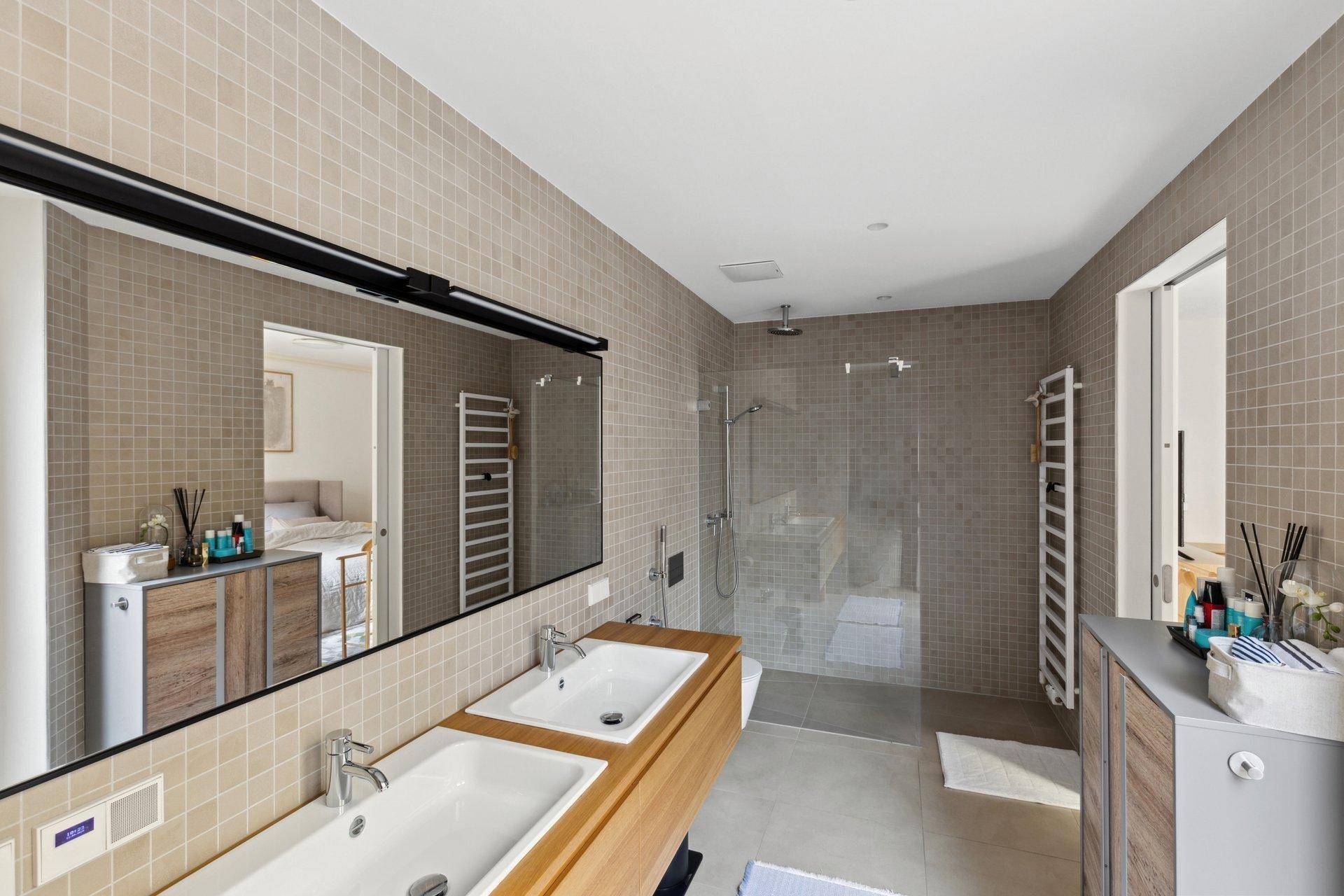 Modernes Badezimmer mit doppelten Waschbecken, begehbarer Dusche und beigefarbenen Mosaikfliesen.