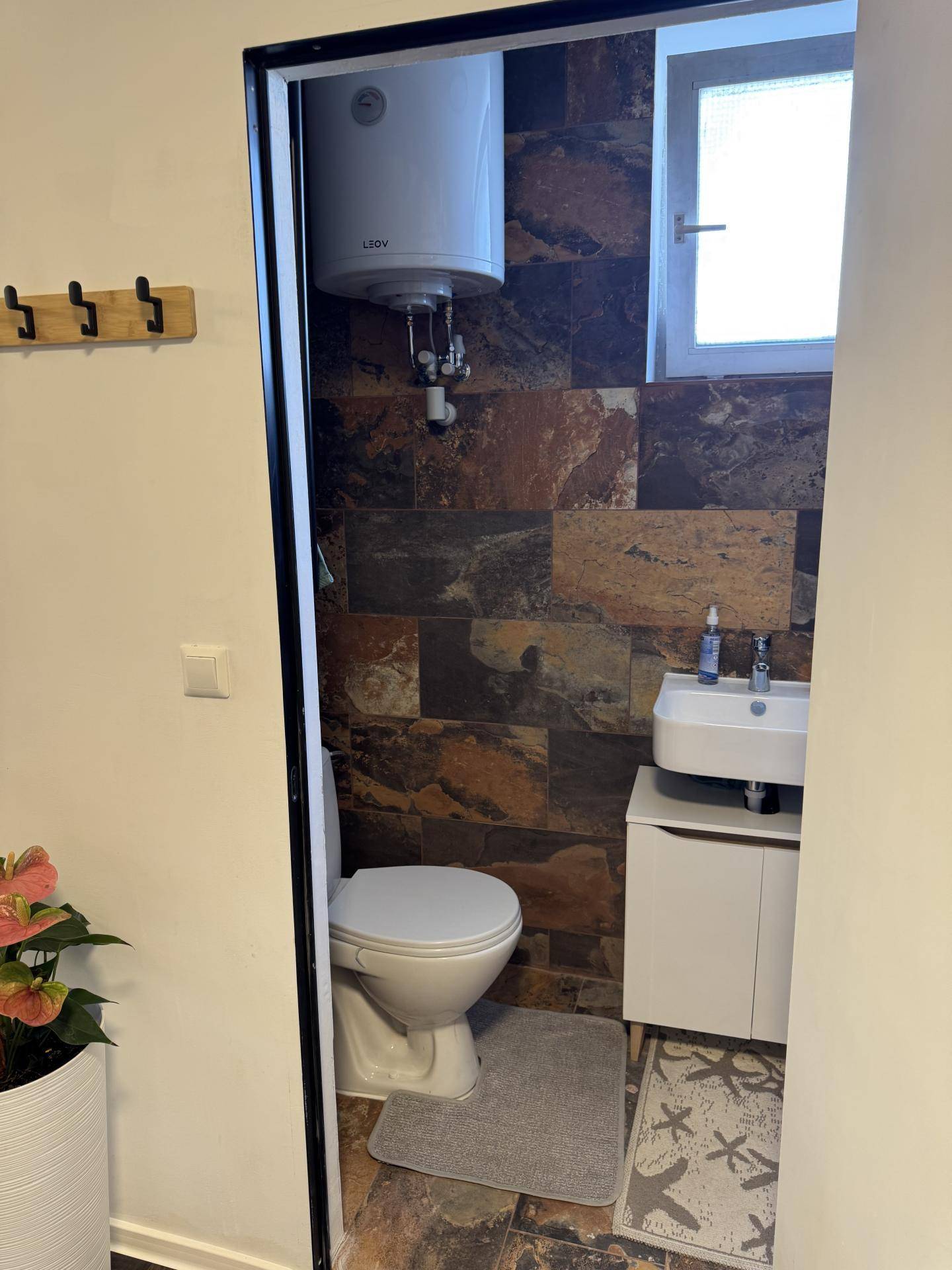 Kleines Gäste-WC mit modern gefliesten Wänden, Fenster und Boiler.