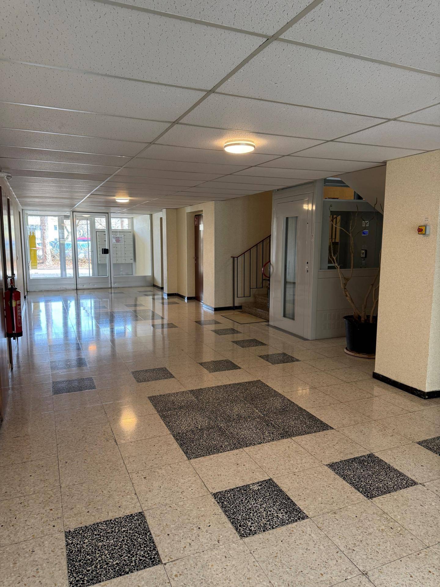 Heller Eingangsbereich eines Mehrfamilienhauses mit Fliesenboden und Aufzug.