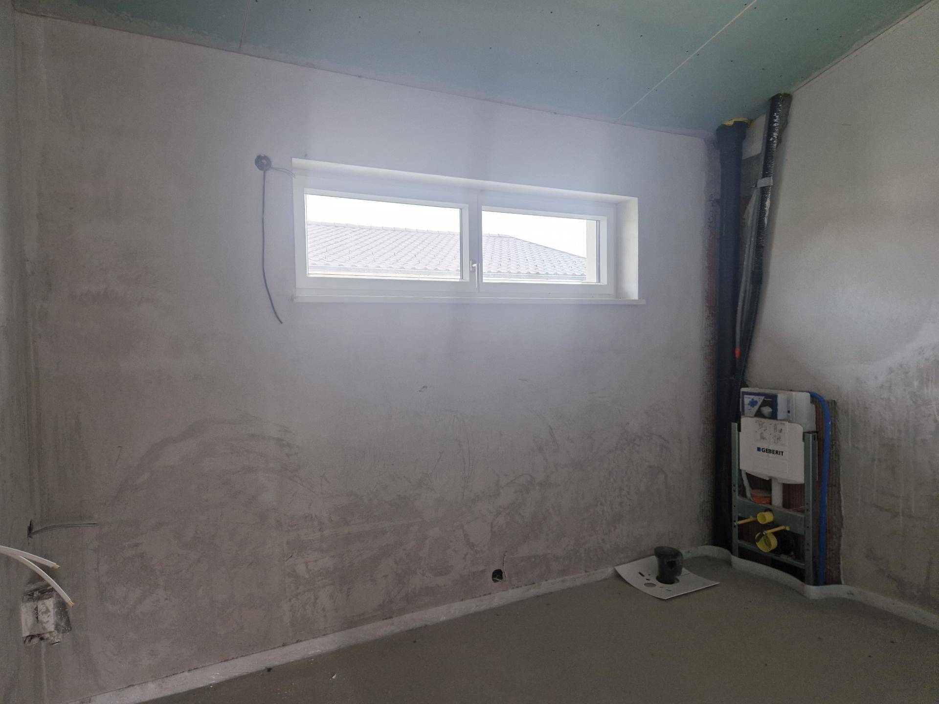 Unfertiges Badezimmer mit einem Fenster und sichtbaren Installationen für die zukünftige Sanitärausstattung.