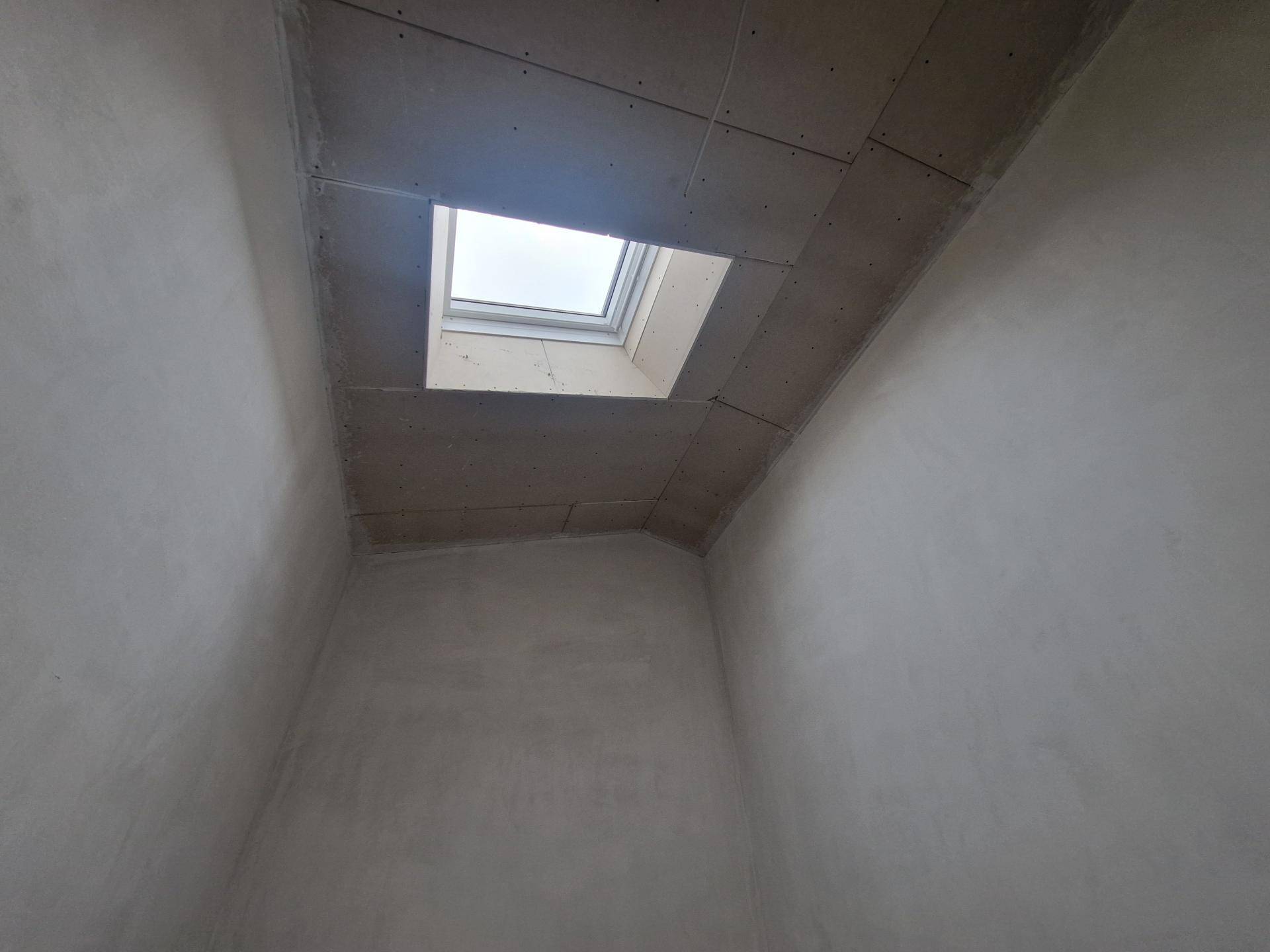 Rohbauzimmer mit einem Dachfenster, das zusätzliches Tageslicht von oben in den Raum bringt.