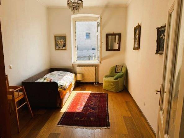 Helles Schlafzimmer mit Holzboden, einem Einzelbett und einem Fenster, das viel Tageslicht hereinlässt.