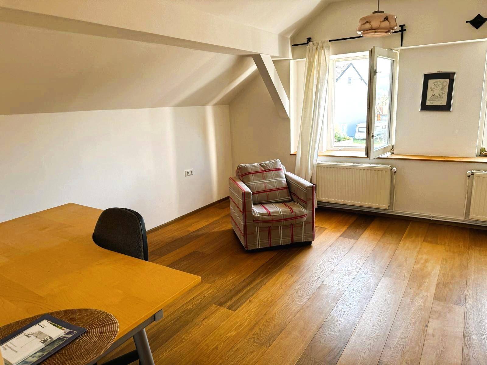 Helles Dachgeschosszimmer mit Holzboden, Schreibtisch und einem Sessel, ideal als Arbeitszimmer.
