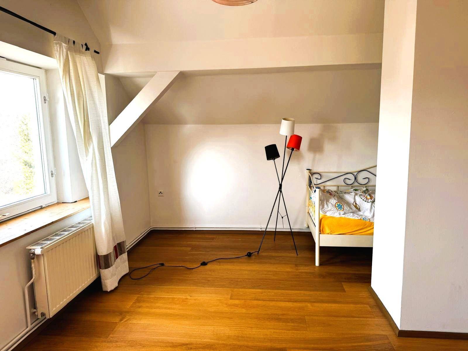 Helles Schlafzimmer im Dachgeschoss mit Holzboden, einem Bett und einem Fenster für Tageslicht.