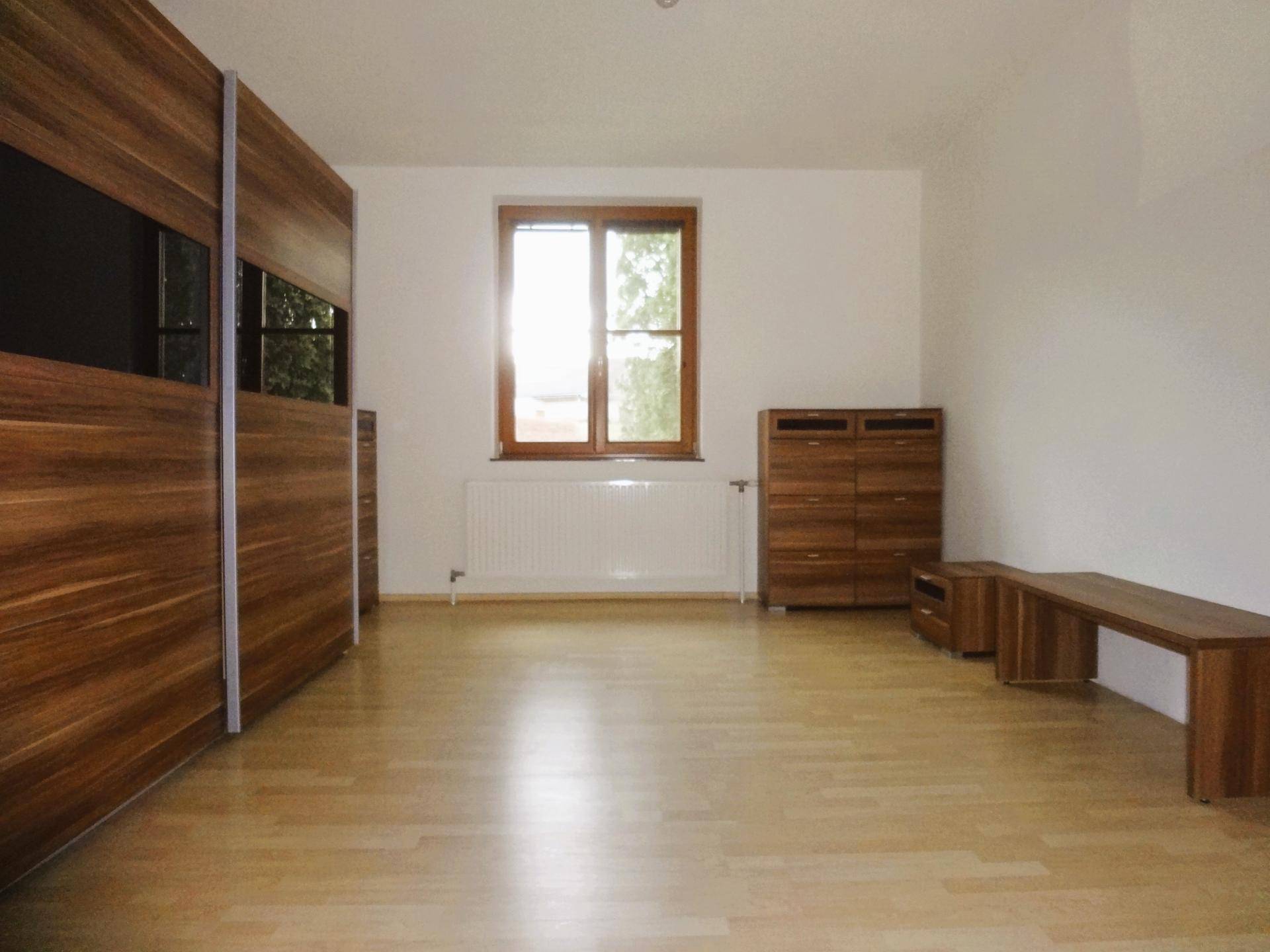 Schlafzimmer mit Holzschrank, Parkettboden und Fenster für natürliches Licht.