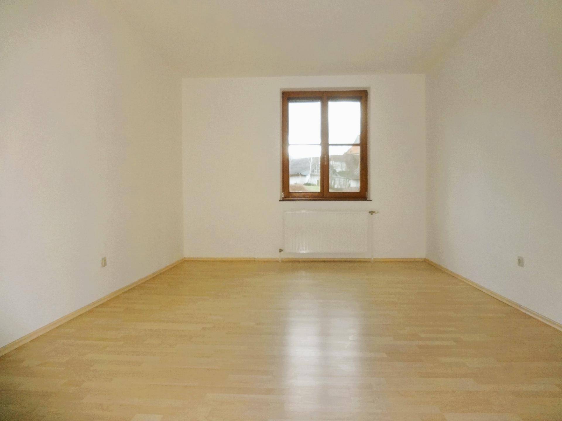 Leeres Zimmer mit Parkettboden und einem Fenster, das viel Licht hereinlässt.