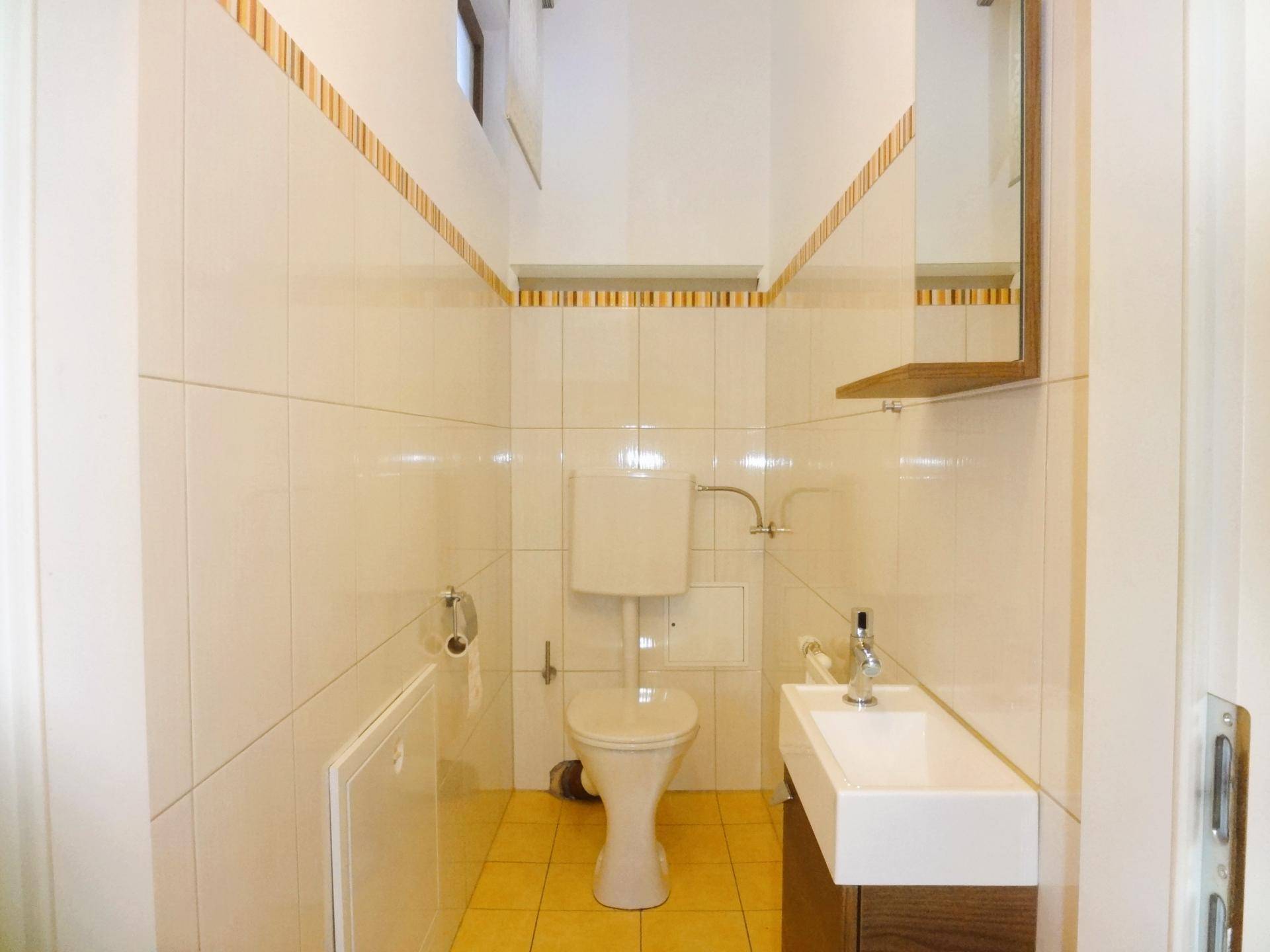 Separate Gästetoilette mit WC, kleinem Waschbecken und Fliesenboden.