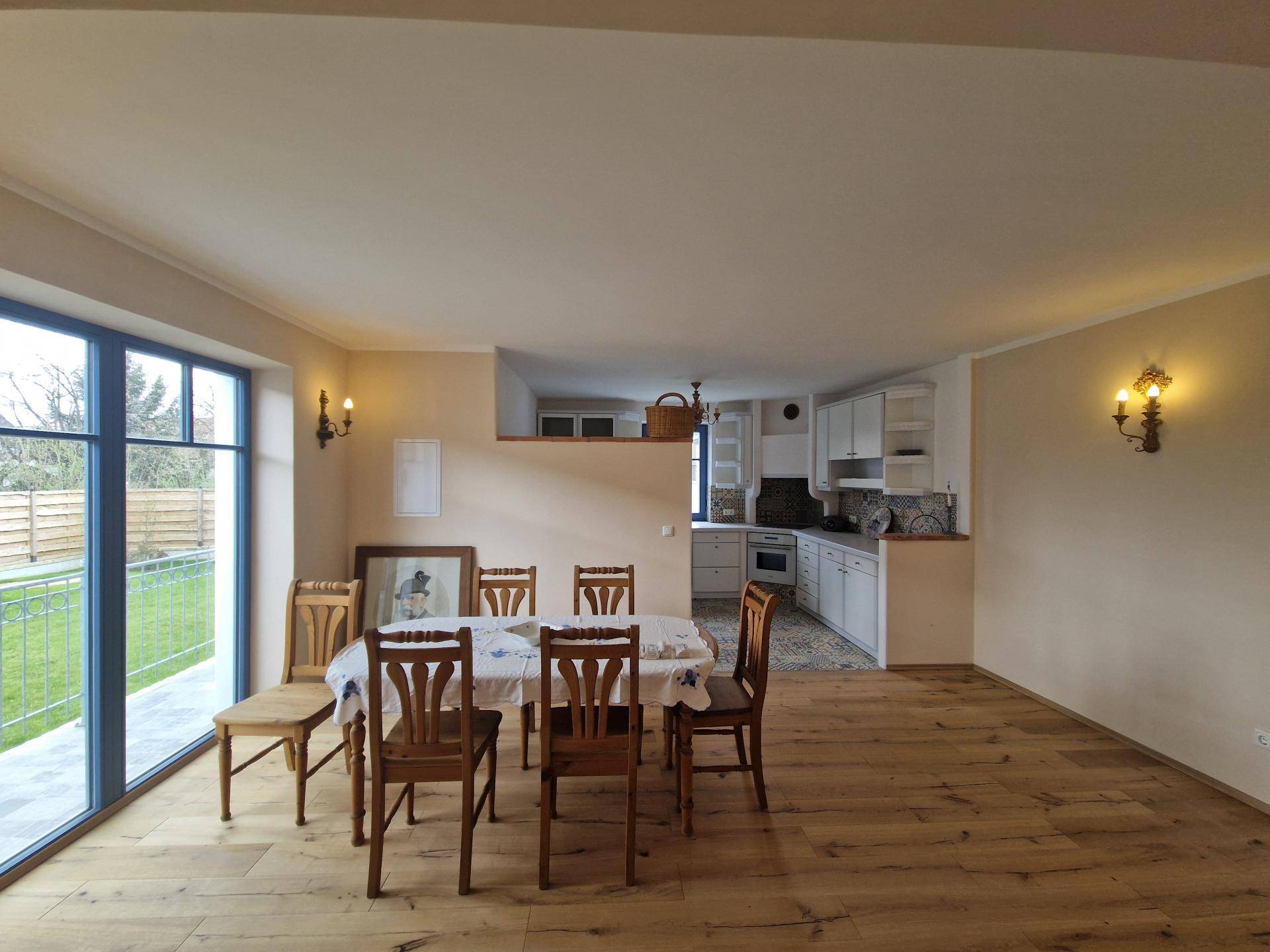 Helles Esszimmer mit Holzboden und Blick auf den Garten, angrenzend an eine offene Küche.