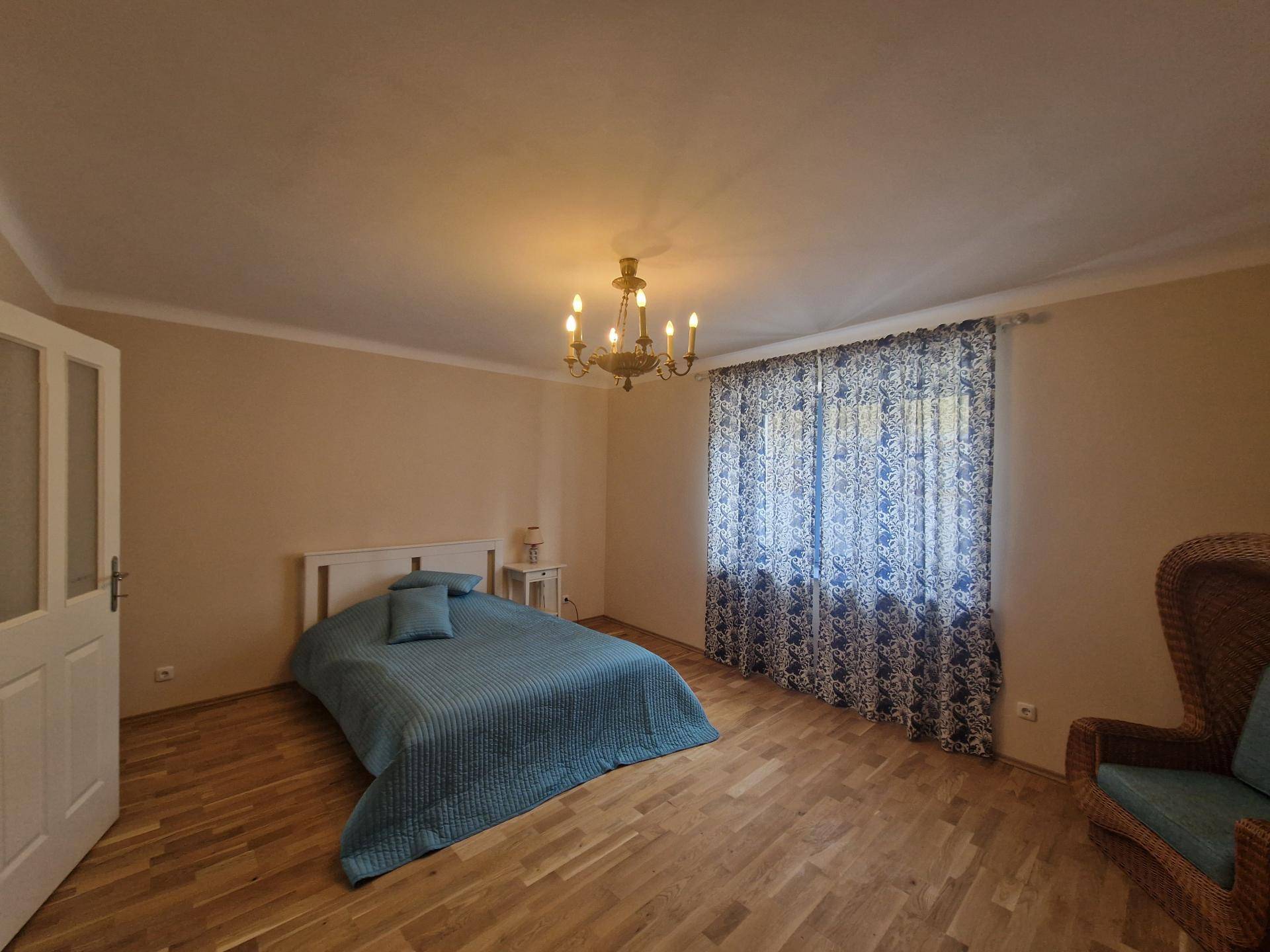 Gemütliches Schlafzimmer mit Holzboden, Doppelbett und dekorativen Vorhängen.