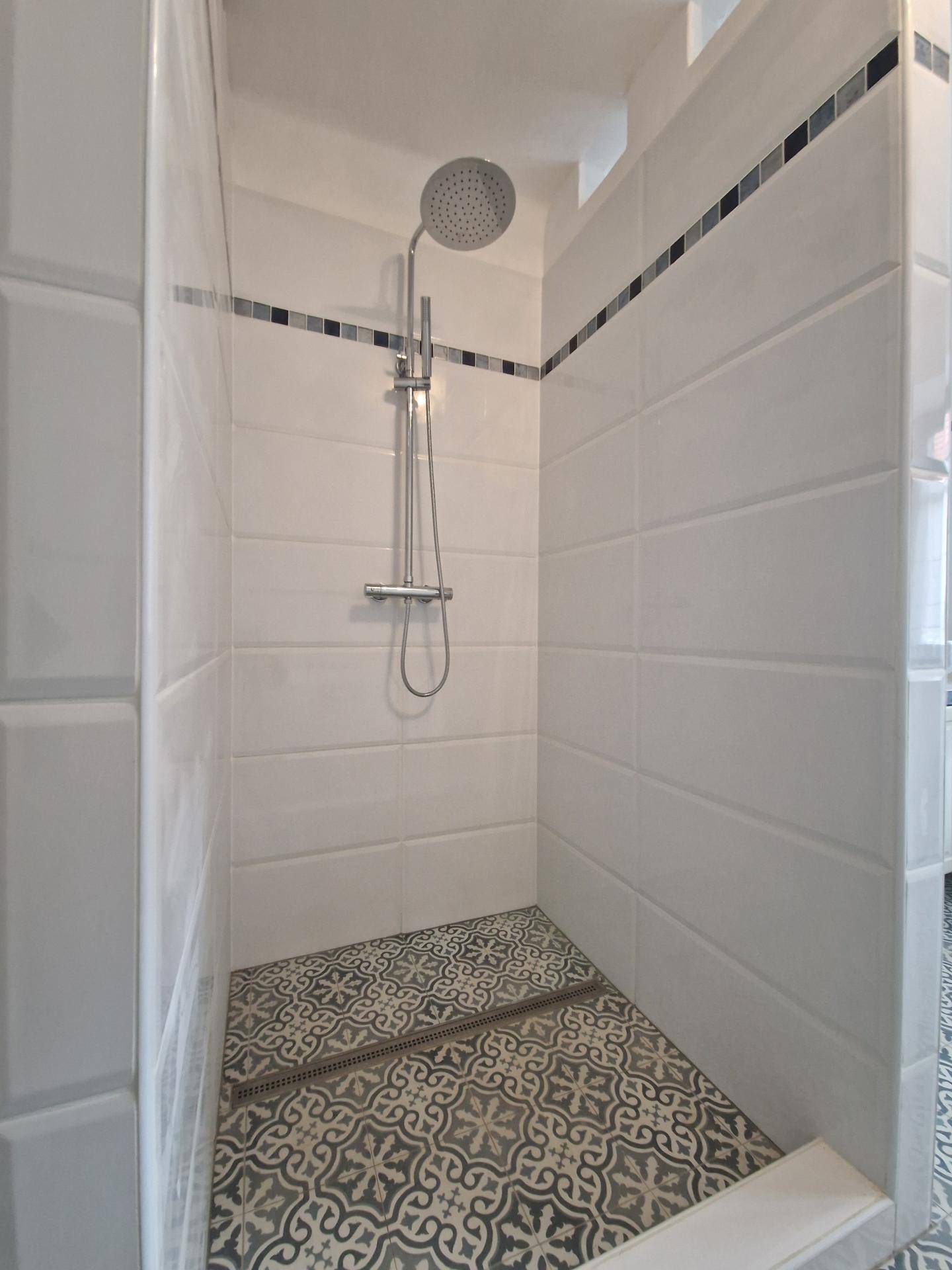 Moderne Duschkabine mit Regenduschkopf und gemusterten Bodenfliesen.
