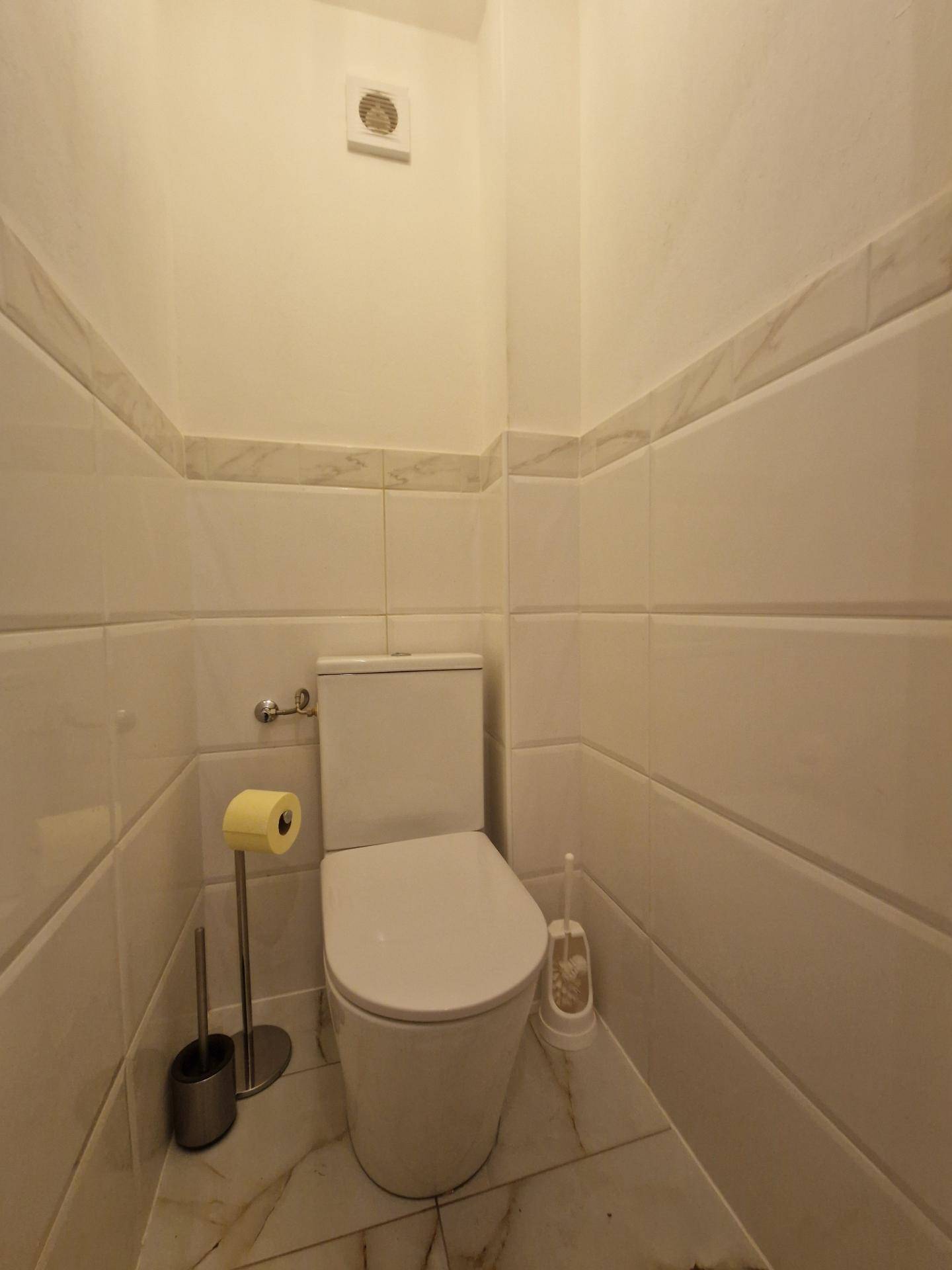 Kleines WC mit weißen Fliesen und einfacher Toilette.