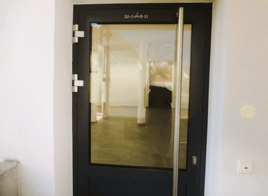 Eingangstür aus Glas und Metall, die in einen hellen, leeren Innenraum führt.