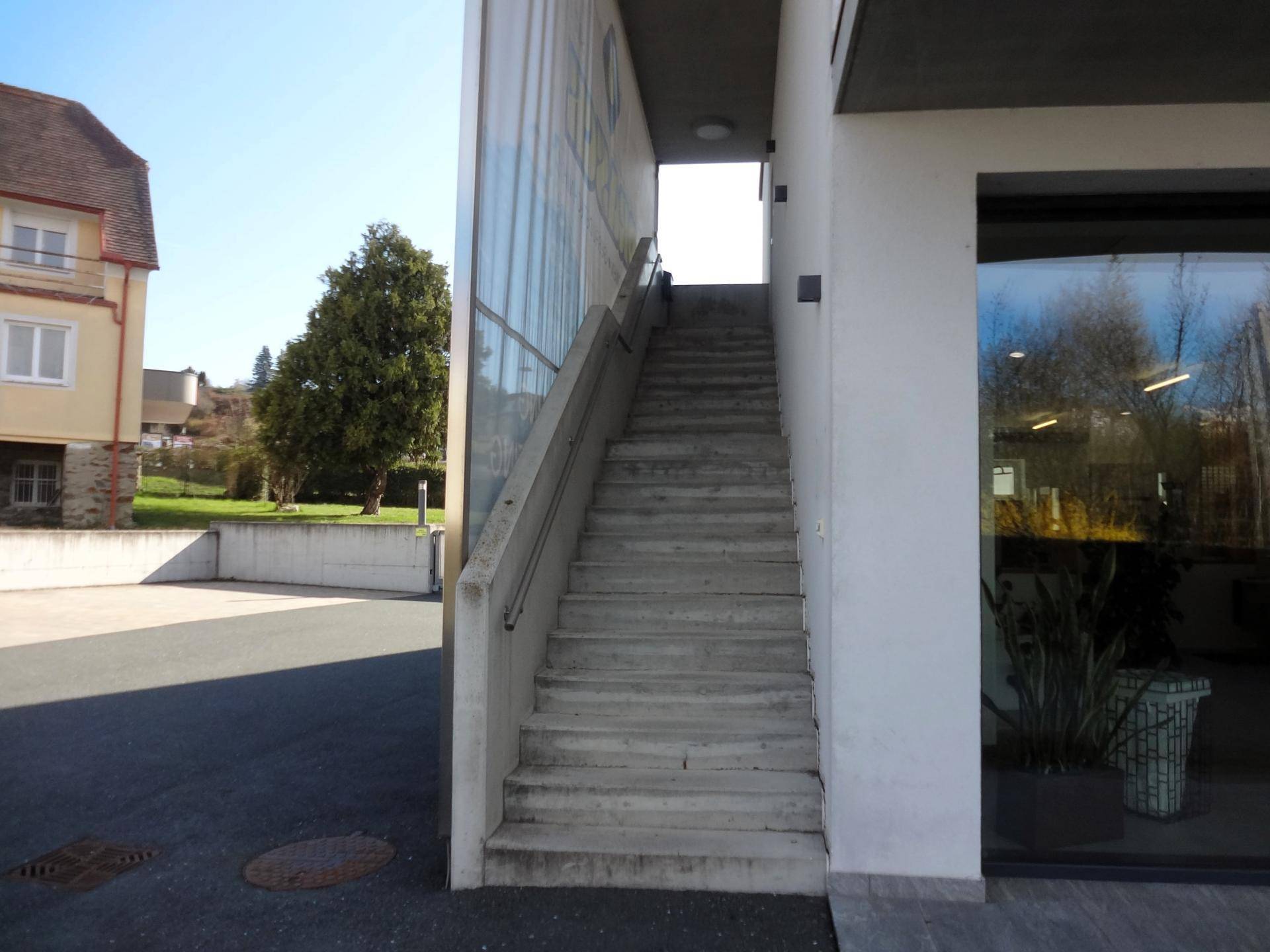Außentreppe aus Beton mit Geländer, die zum Eingang eines modernen Gebäudes führt.