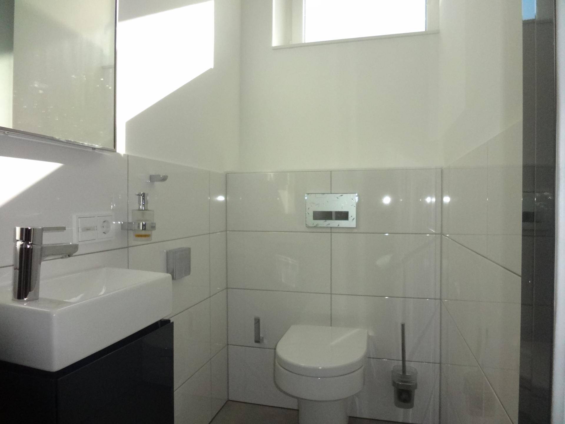 Modernes Gäste-WC mit wandhängender Toilette, kleinem Waschbecken und Fenster für Tageslicht.