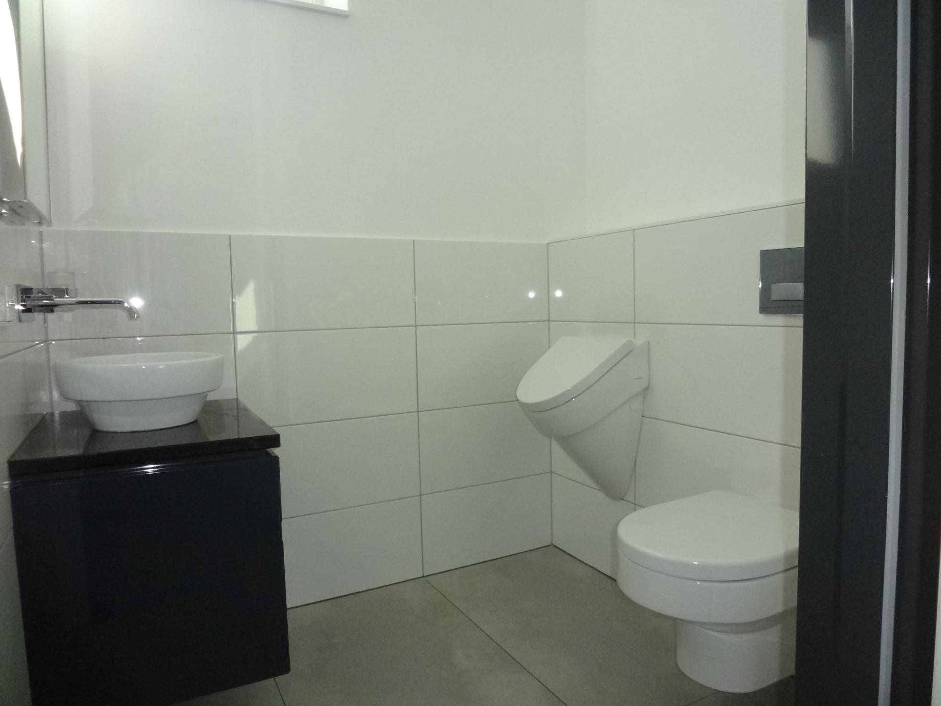 Helles Badezimmer mit modernem Urinal, wandhängender Toilette und kleinem Aufsatzwaschbecken.