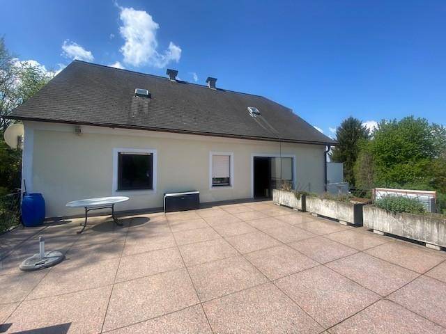 Rückseite des Hauses mit großer gepflasterter Terrasse unter blauem Himmel.
