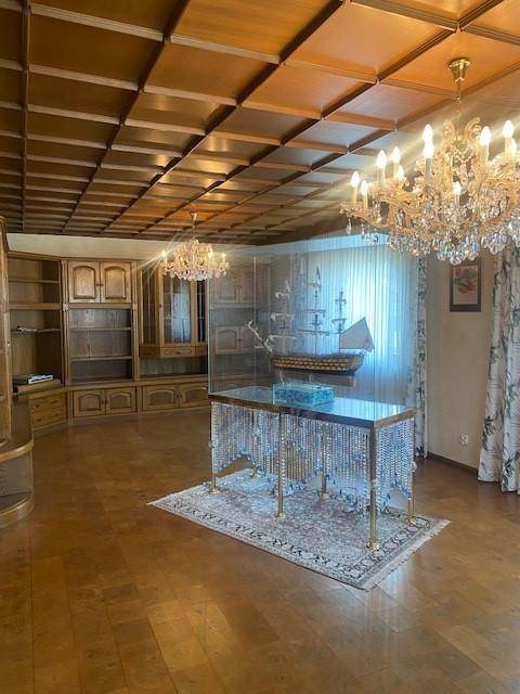 Geräumiges Wohnzimmer mit Holzkassettendecke, Parkettboden und eleganten Kristallleuchtern.