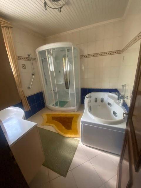 Badezimmer mit Duschkabine, Eck-Whirlpool und Fliesenboden, ausgestattet mit Haltegriffen.