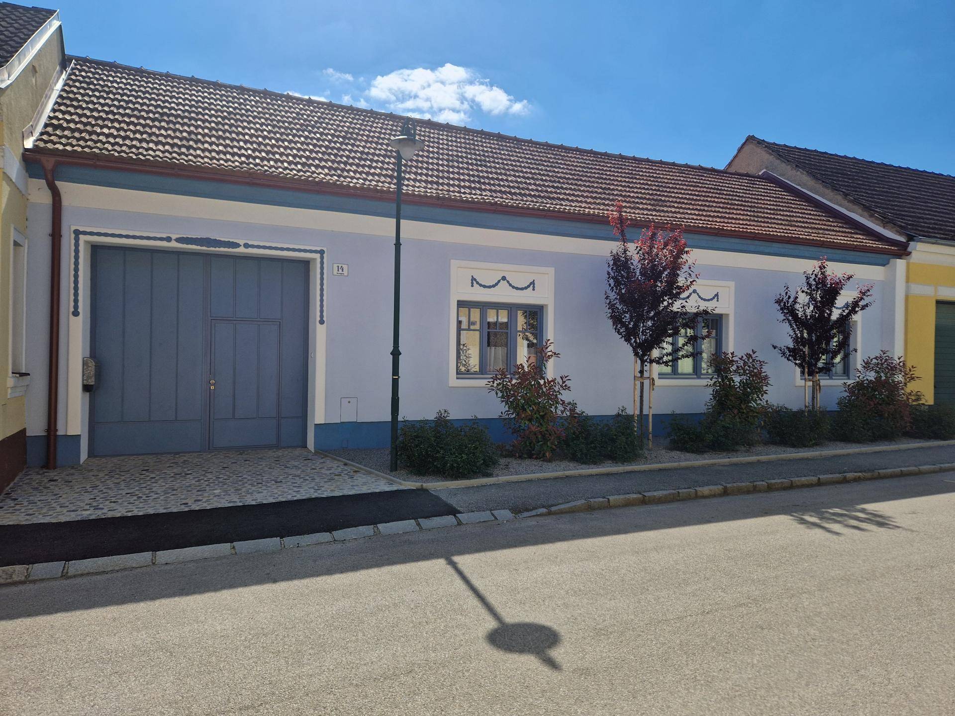 Traditionelles Haus mit blauer Fassade, großem Garagentor und gepflegtem Vorgarten.