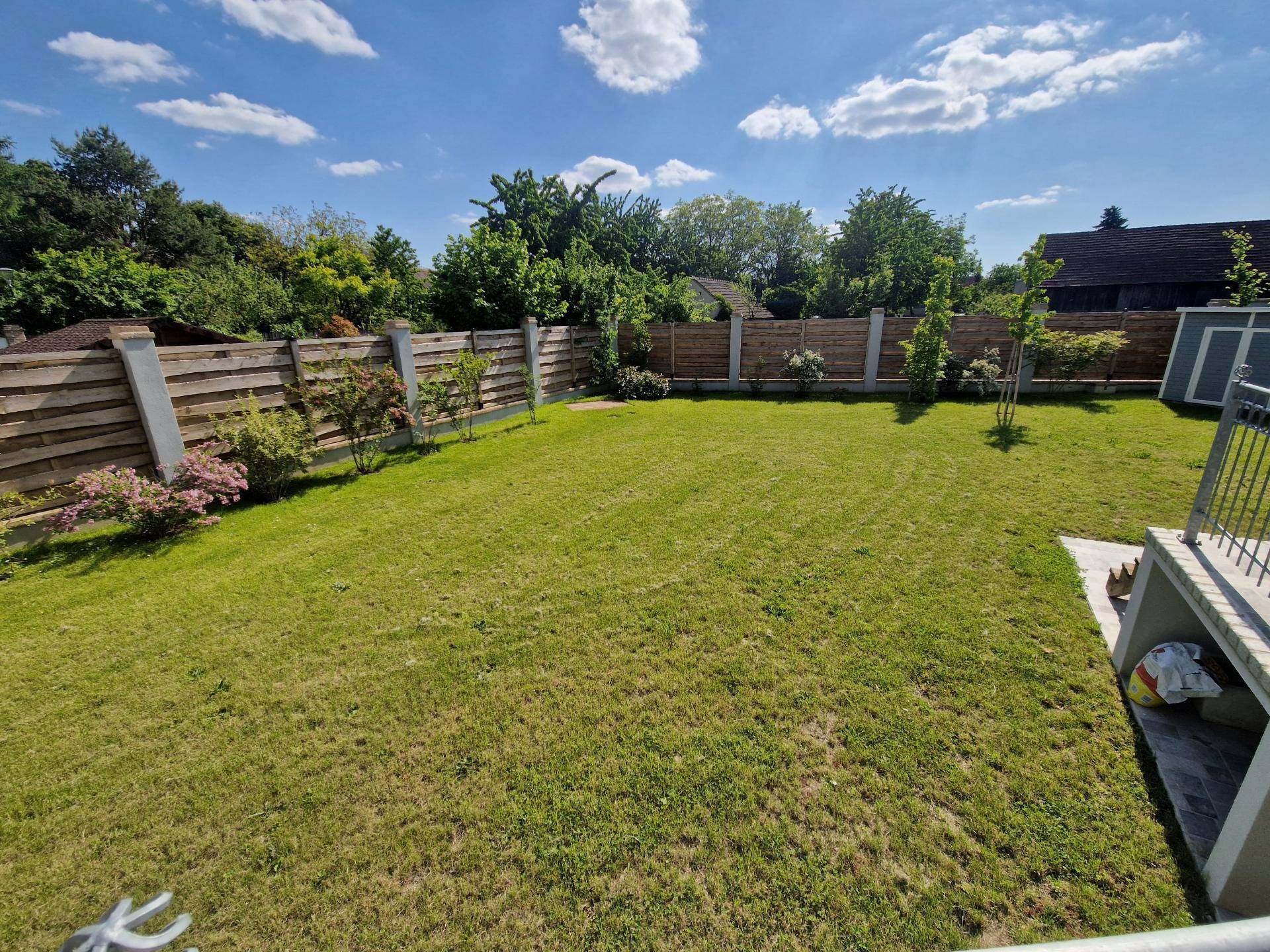 Großer, gepflegter Garten mit Rasenfläche und Holzzaun unter blauem Himmel.