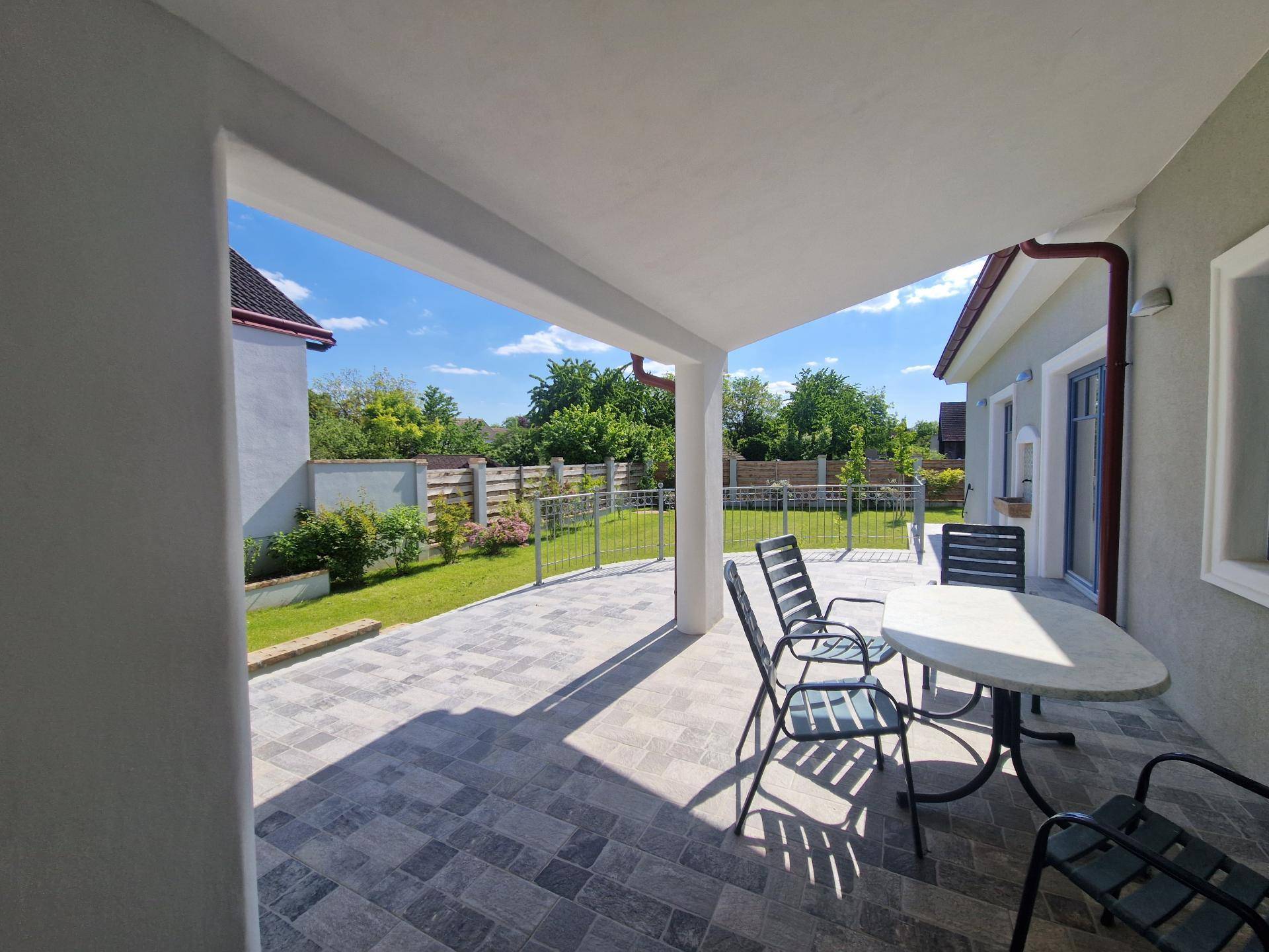 Gemütliche überdachte Terrasse mit Gartenmöbeln und Blick ins Grüne an einem sonnigen Tag.