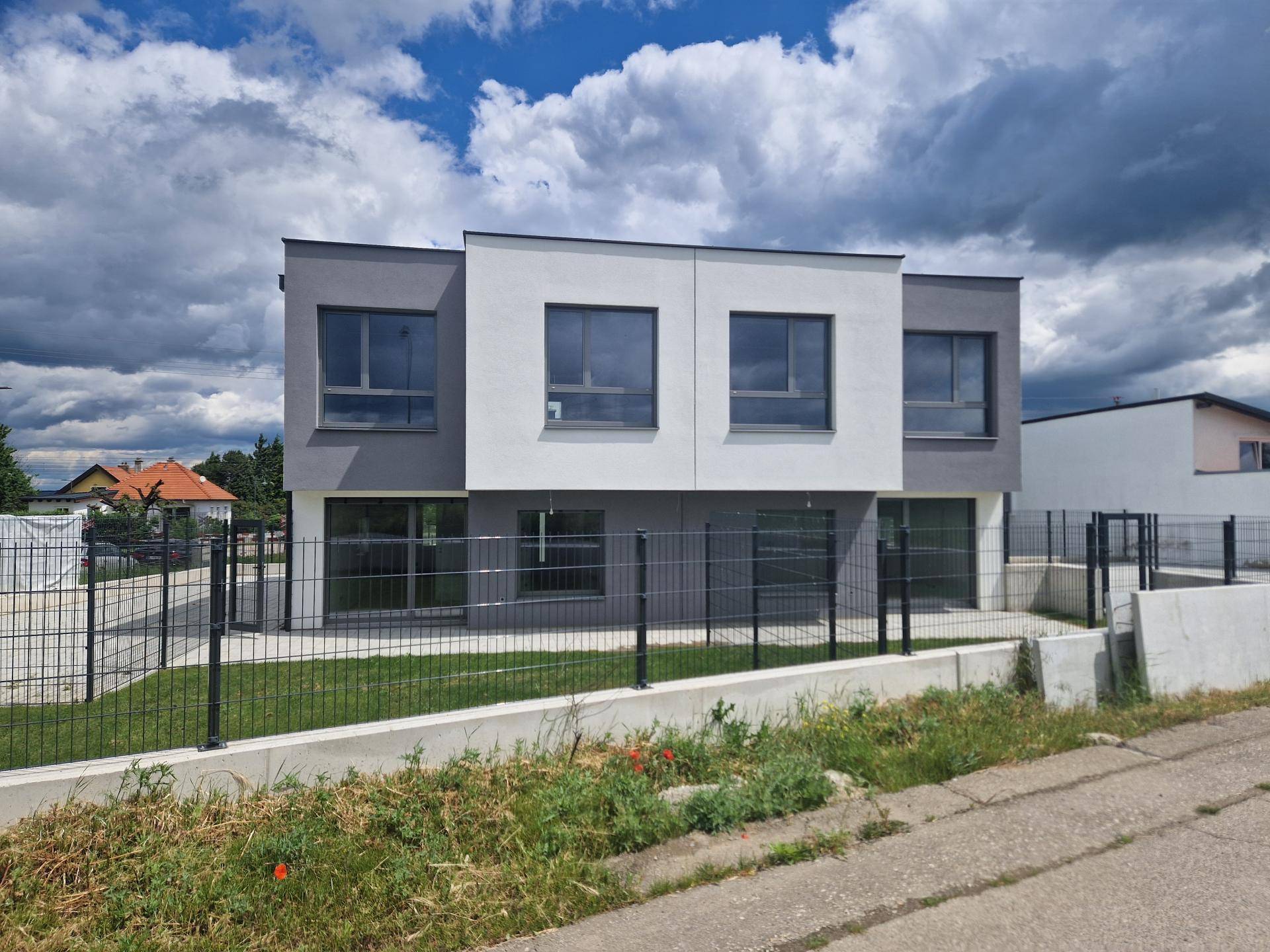 Moderne Reihenhäuser mit weißer und grauer Fassade unter bewölktem Himmel.