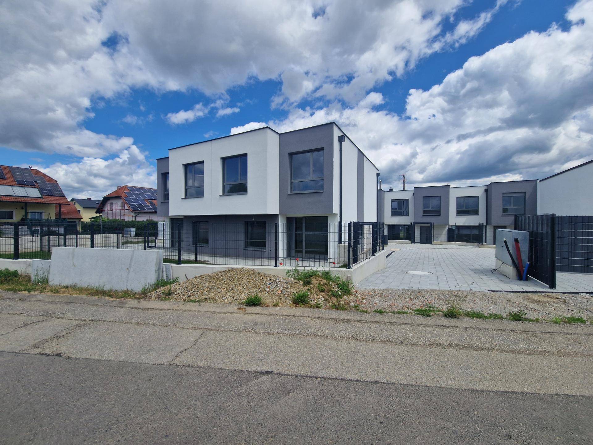 Reihe moderner Häuser mit grauen und weißen Fassaden und gepflastertem Vorplatz.