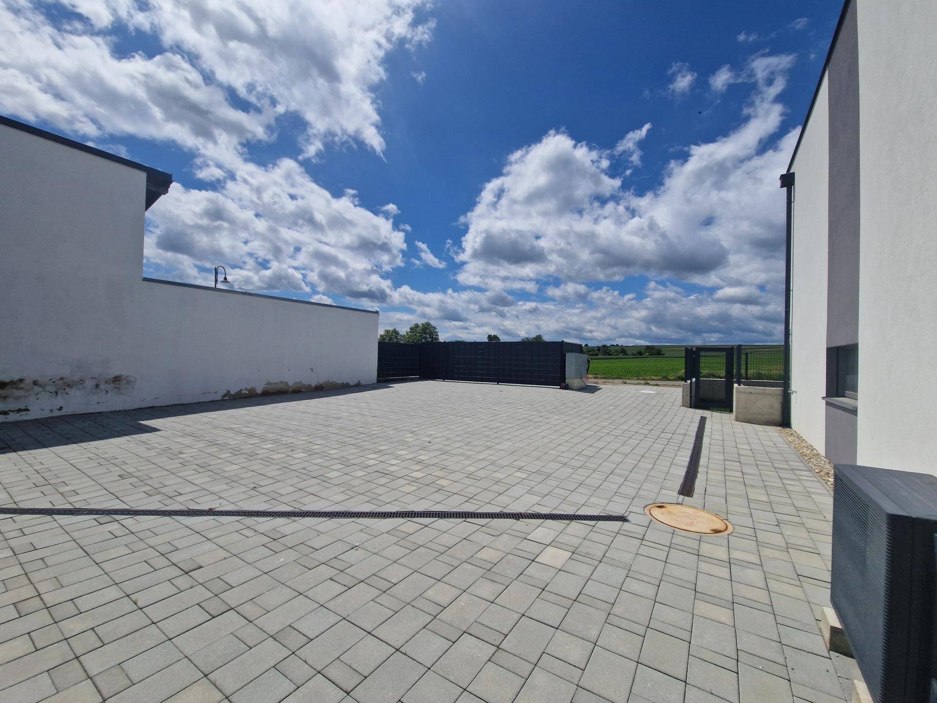 Großer gepflasterter Außenbereich mit weitem Blick auf grüne Felder unter blauem Himmel.