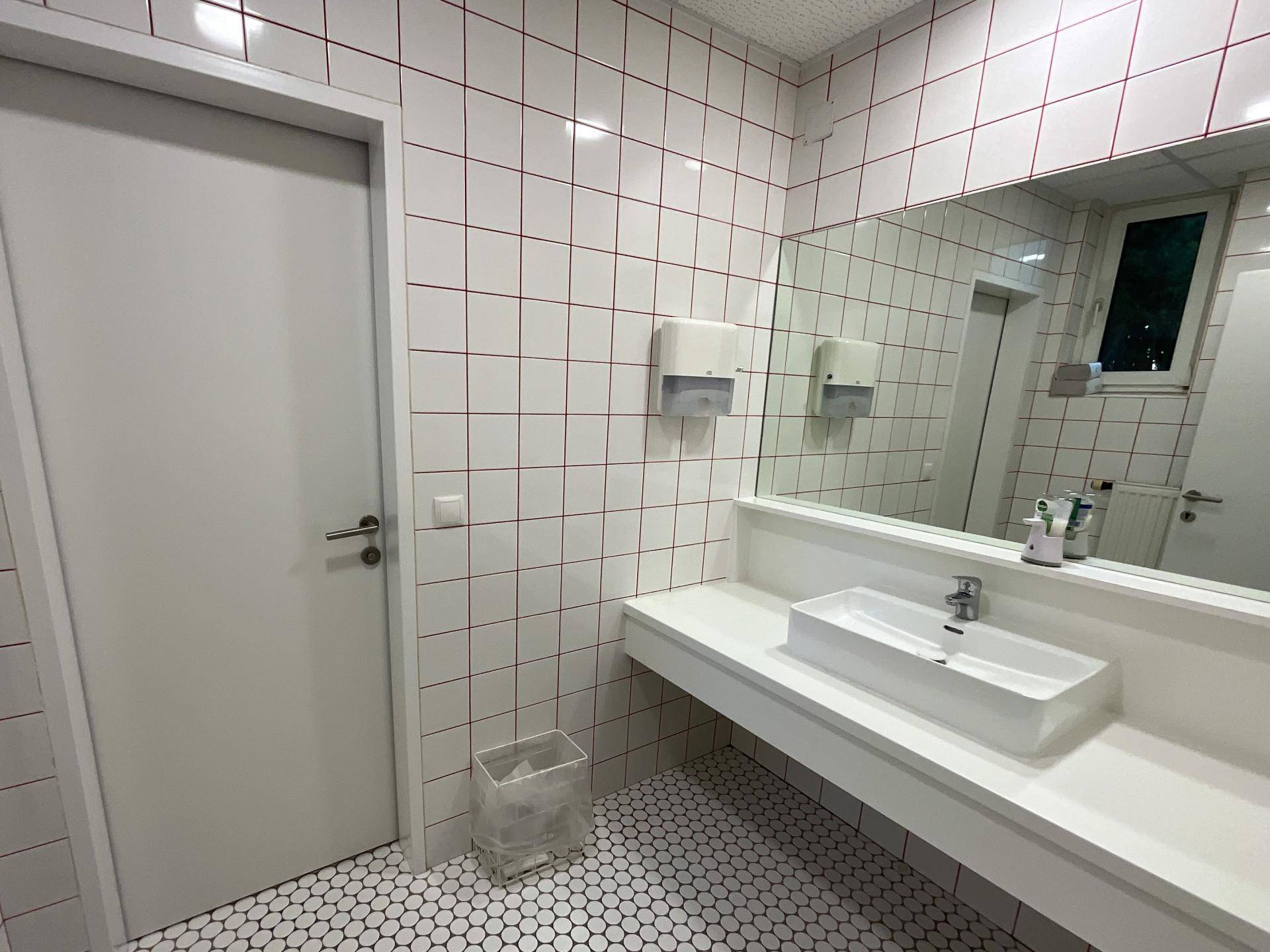 Modernes Badezimmer mit weißen Fliesen, einem großen Spiegel und einem Waschbecken auf einer langen Ablage.