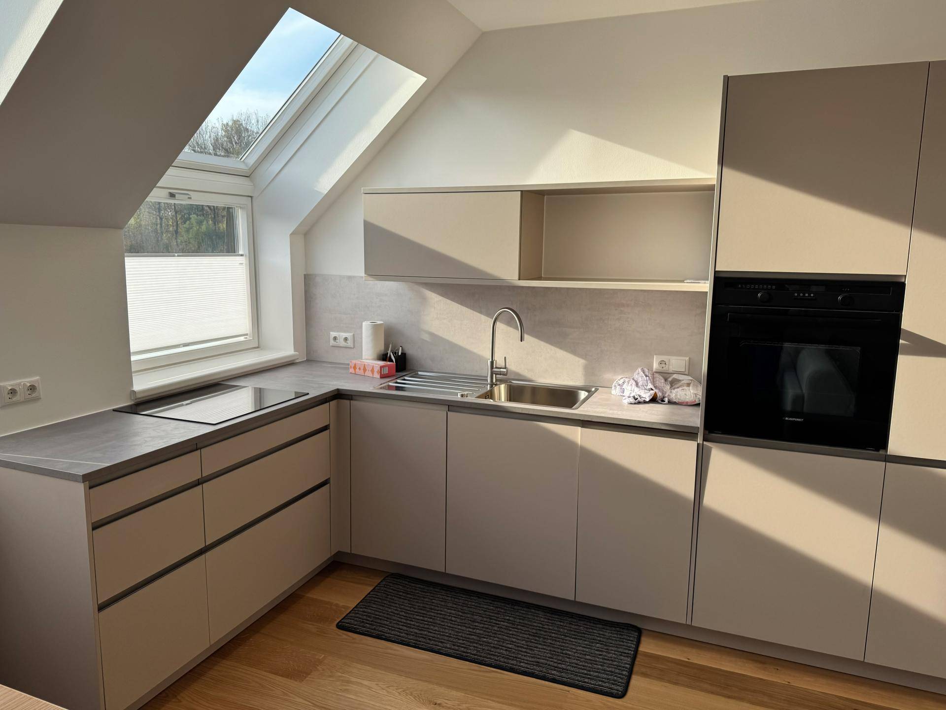 Moderne Einbauküche in einem Dachgeschoss mit Schrägdach, Induktionskochfeld, Backofen und hellem Holzfußboden.