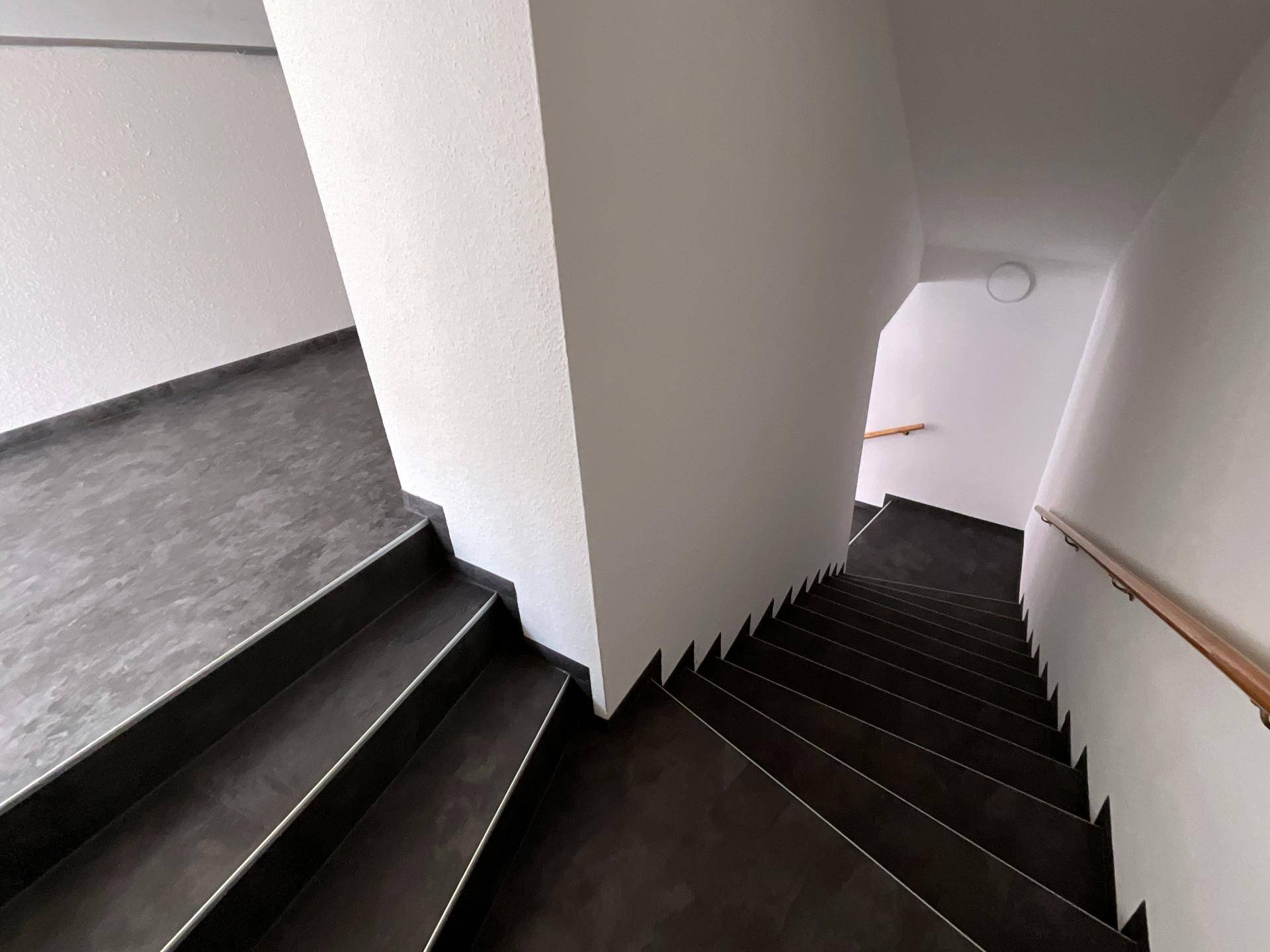 Modernes Treppenhaus mit dunklen Stufen und hellem Geländer, das zu den oberen Etagen führt.