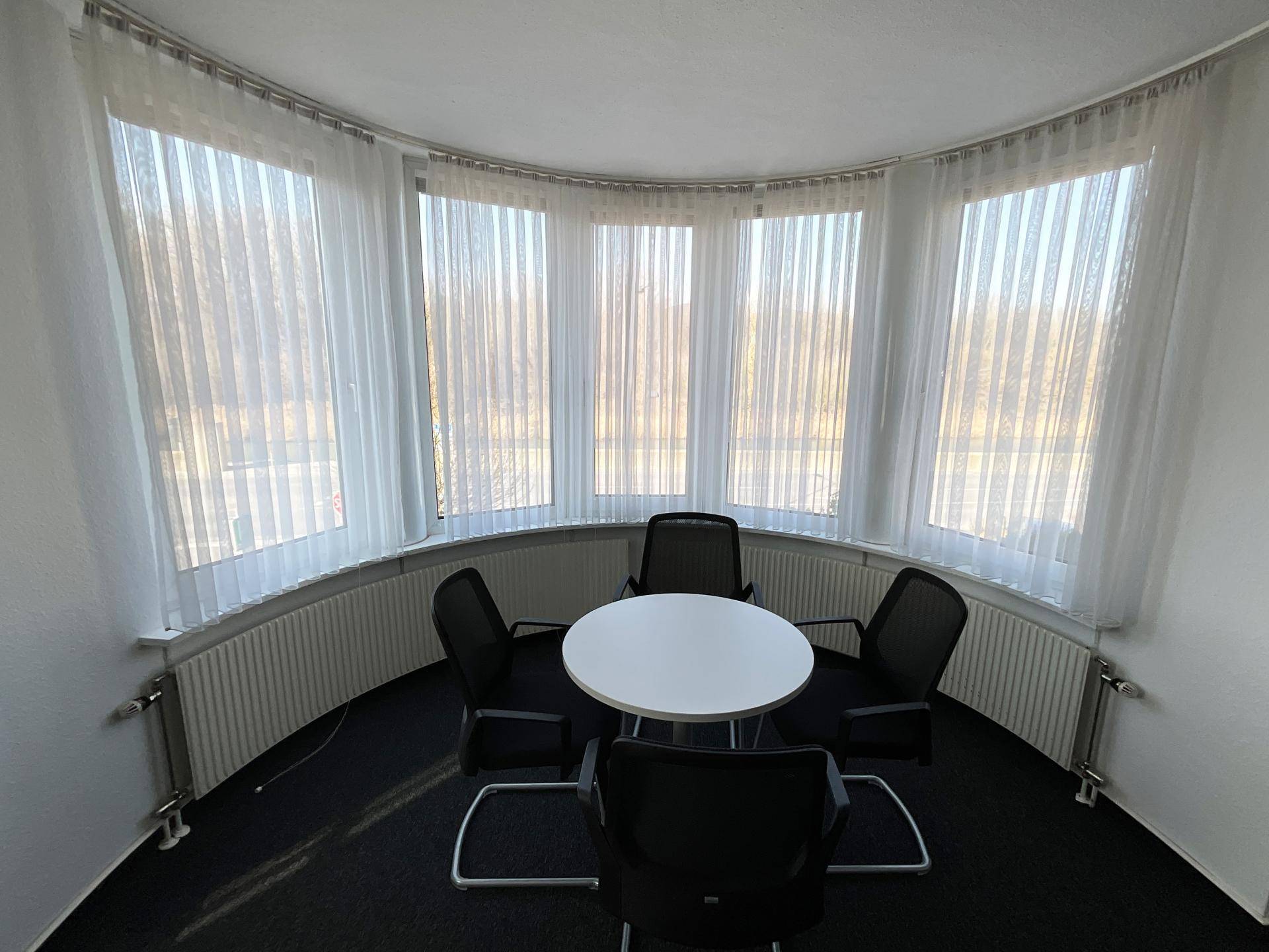 Runder Besprechungsraum mit großen Fenstern, die viel Tageslicht hereinlassen, und einem runden Tisch.