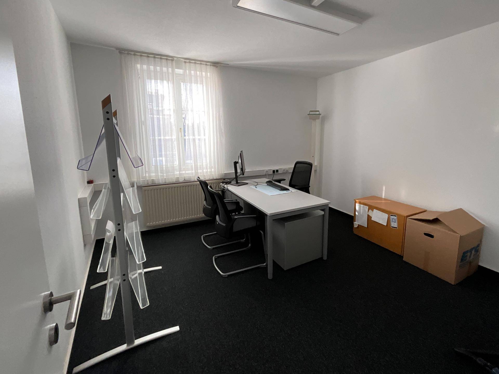 Kleines Büro mit einem Arbeitsplatz, einem Fenster und Kartons, die auf einen Umzug hindeuten.