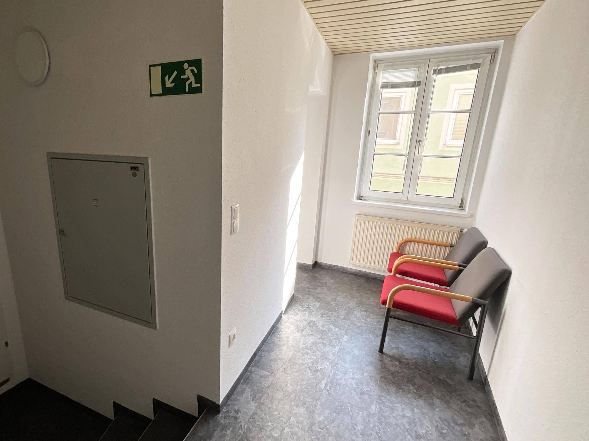 Treppenabsatz mit Fenster, Sitzgelegenheiten und einem Feuerlöscher an der Wand.