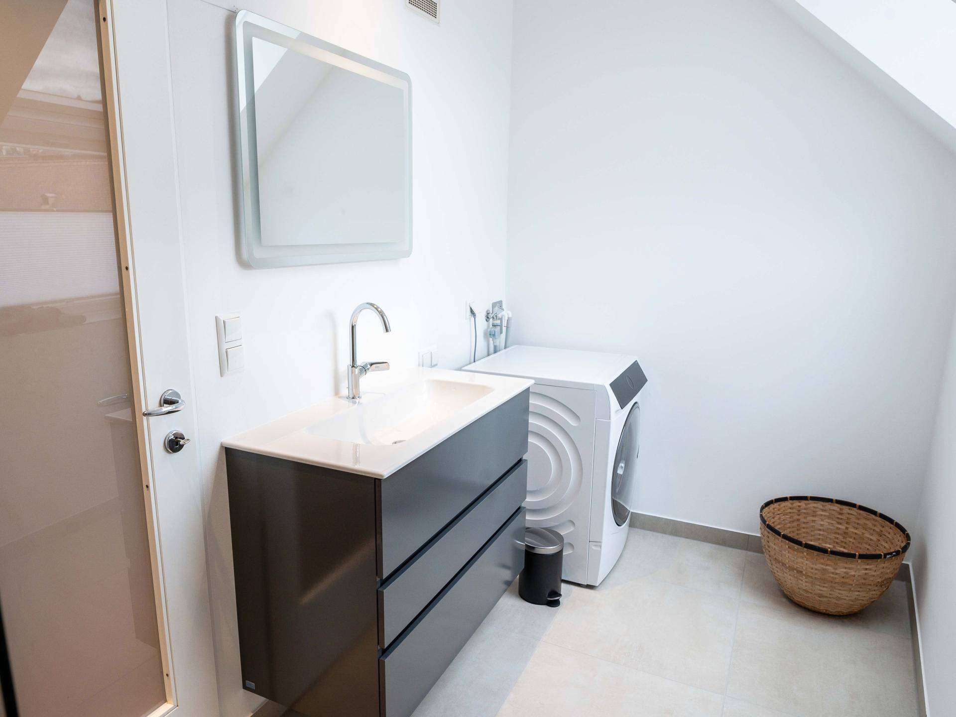 Modernes Badezimmer mit Waschbeckenunterschrank, Waschmaschine und schrägen Wänden im Dachgeschoss.