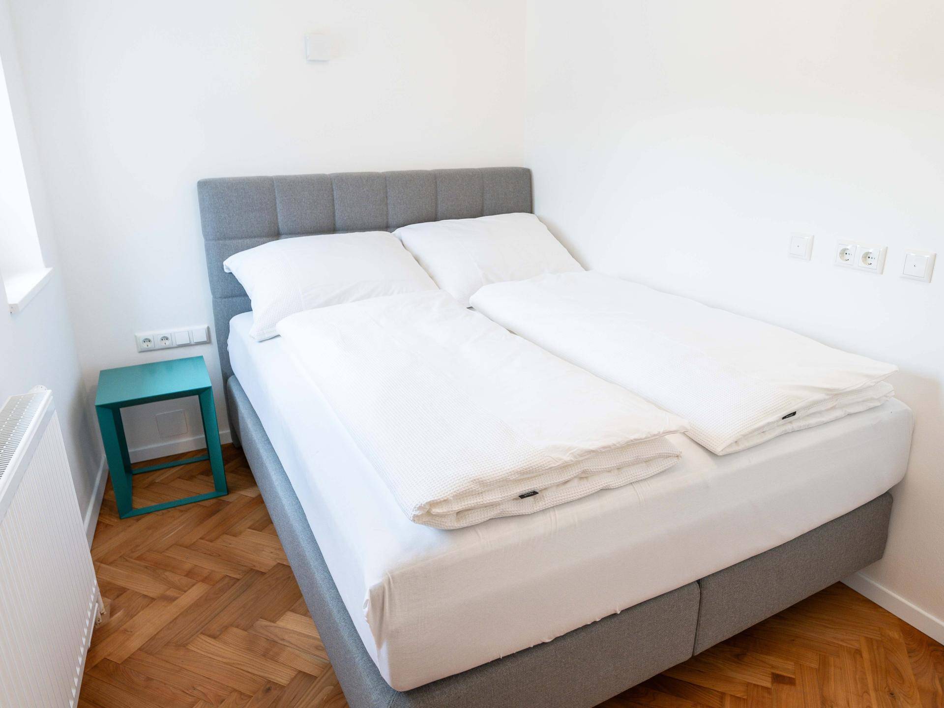 Helles Schlafzimmer mit einem Doppelbett, Holzboden und weißen Wänden, die eine ruhige Atmosphäre schaffen.