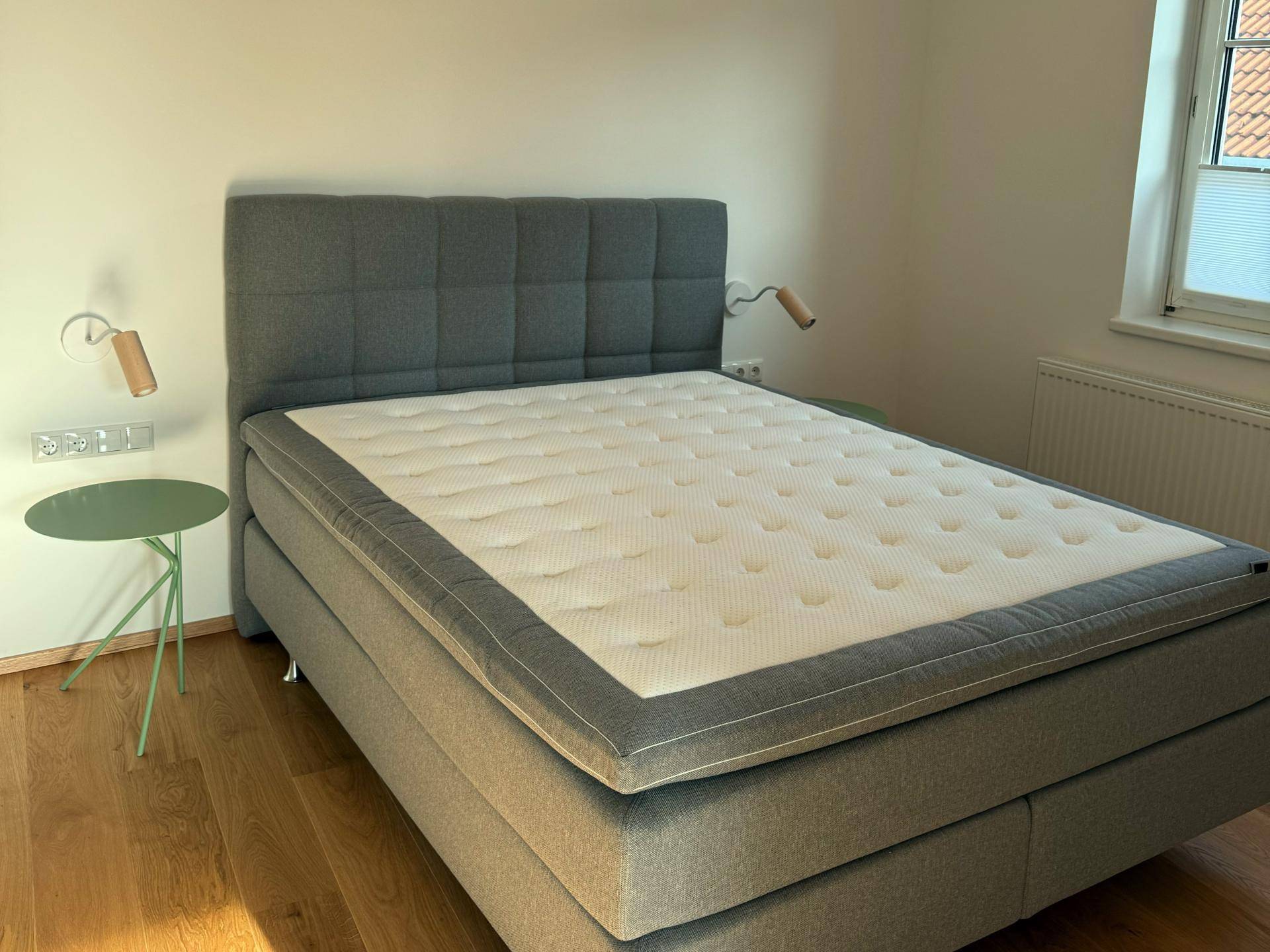 Gemütliches Schlafzimmer mit großem, gepolstertem Bett, kleinem Beistelltisch und Fenster für natürliches Licht.