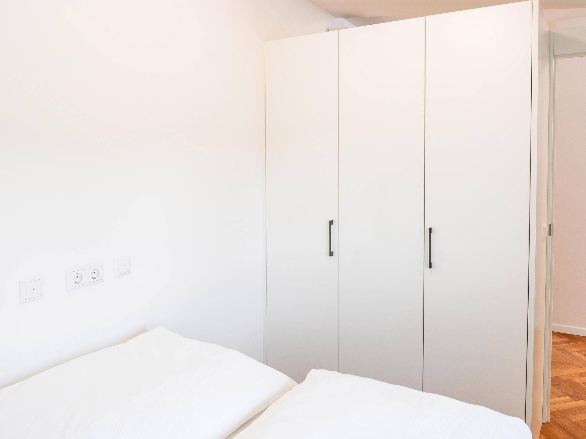 Schlafzimmer mit weißem Kleiderschrank und Holzboden, der eine warme und einladende Atmosphäre schafft.