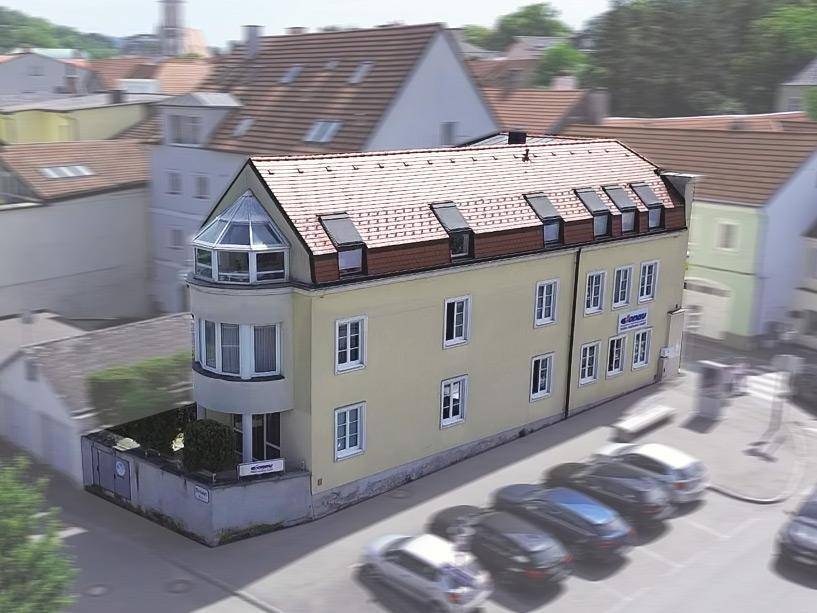 Luftaufnahme eines modernen Gebäudes mit rotem Ziegeldach und markantem Erker, umgeben von Parkplätzen und Hecken.