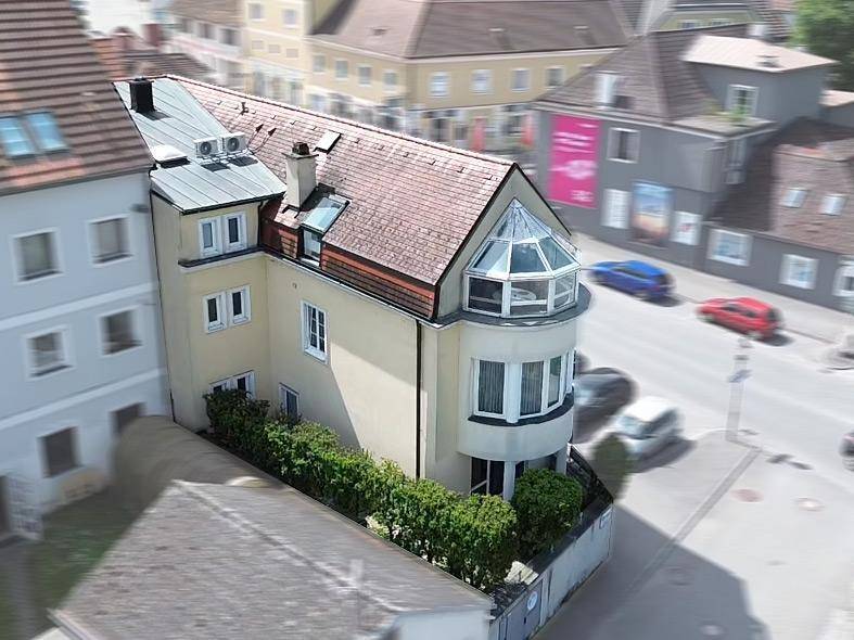 Luftaufnahme eines modernen Gebäudes mit rotem Ziegeldach und markantem Erker, umgeben von Parkplätzen und Hecken.