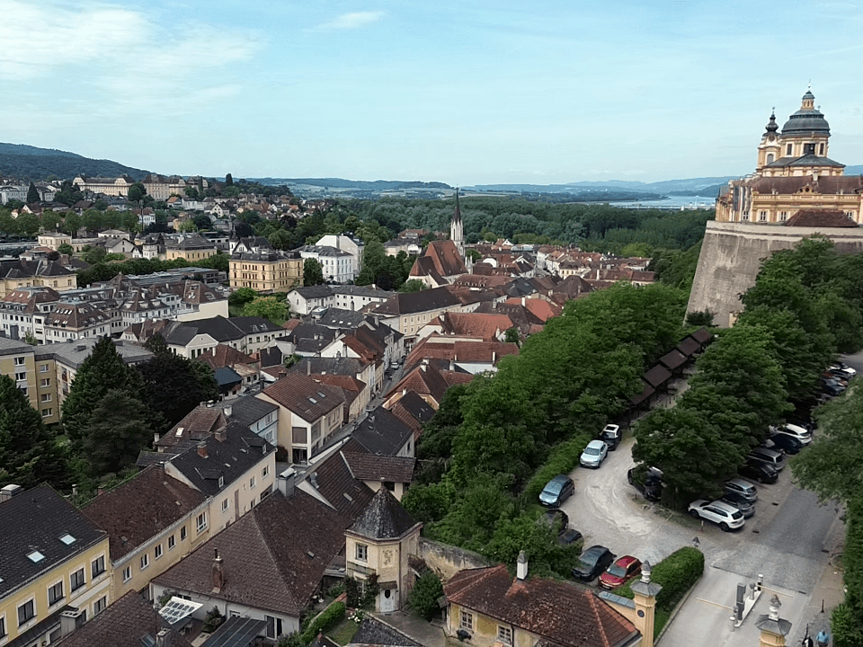 Panoramablick auf eine historische Stadt mit vielen Gebäuden, grünen Flächen und einem Fluss im Hintergrund.