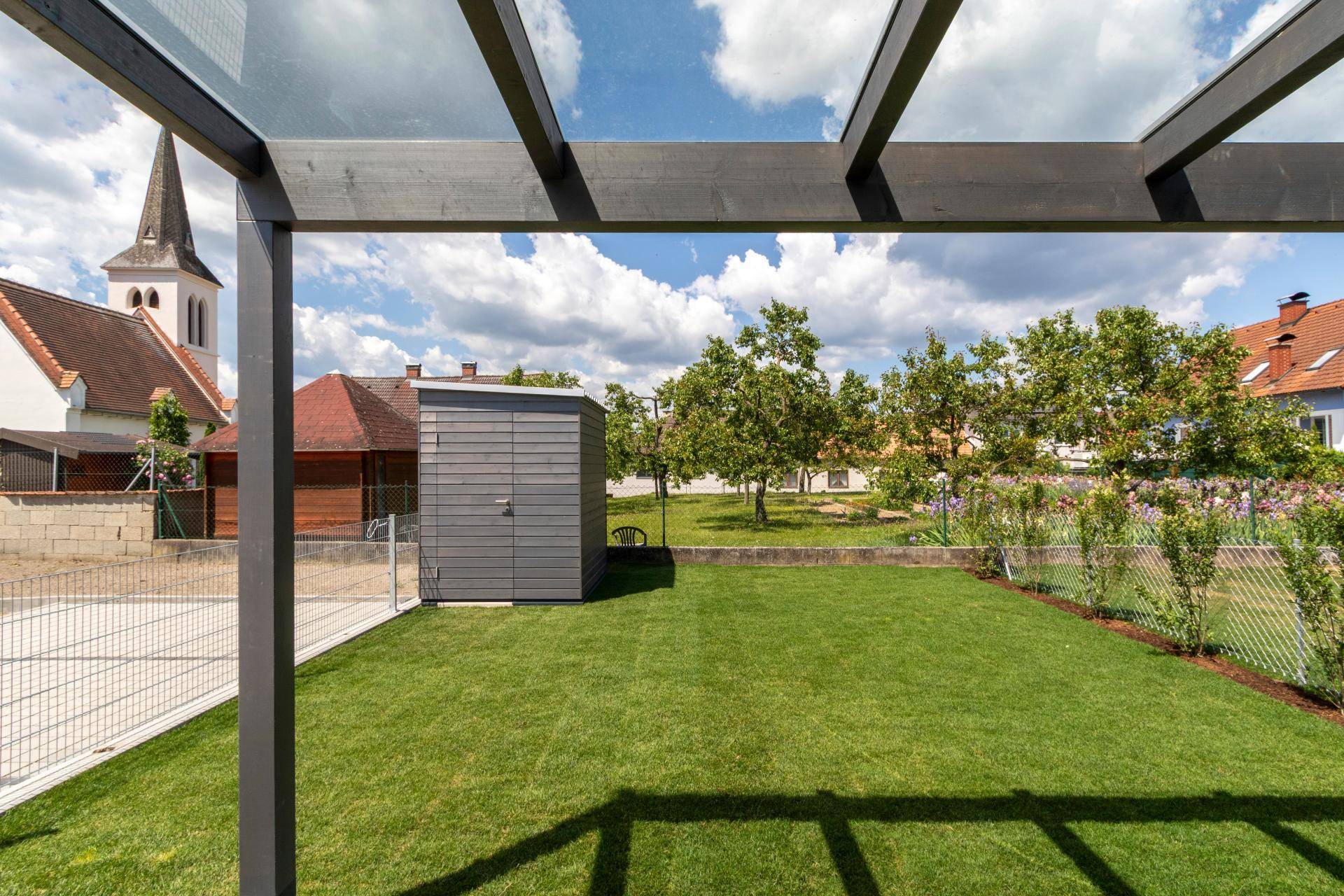 Gepflegter Gartenbereich mit Rasenfläche, Gartenhaus und Blick auf eine nahegelegene Kirche.