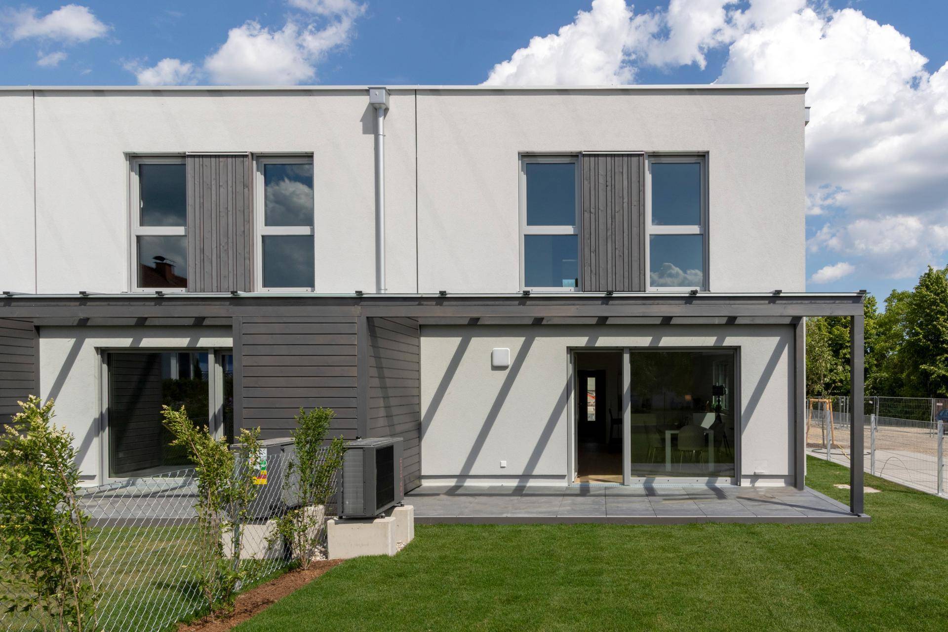 Helle Terrassenbereiche mit Zugang zum Garten und großen Fensterfronten der Reihenhäuser.