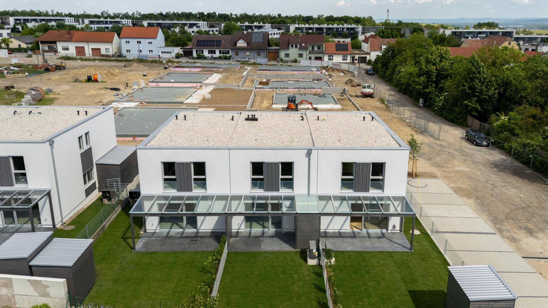 Vogelperspektive auf fertiggestellte Reihenhäuser und die umliegende Baustelle für weitere Wohneinheiten.