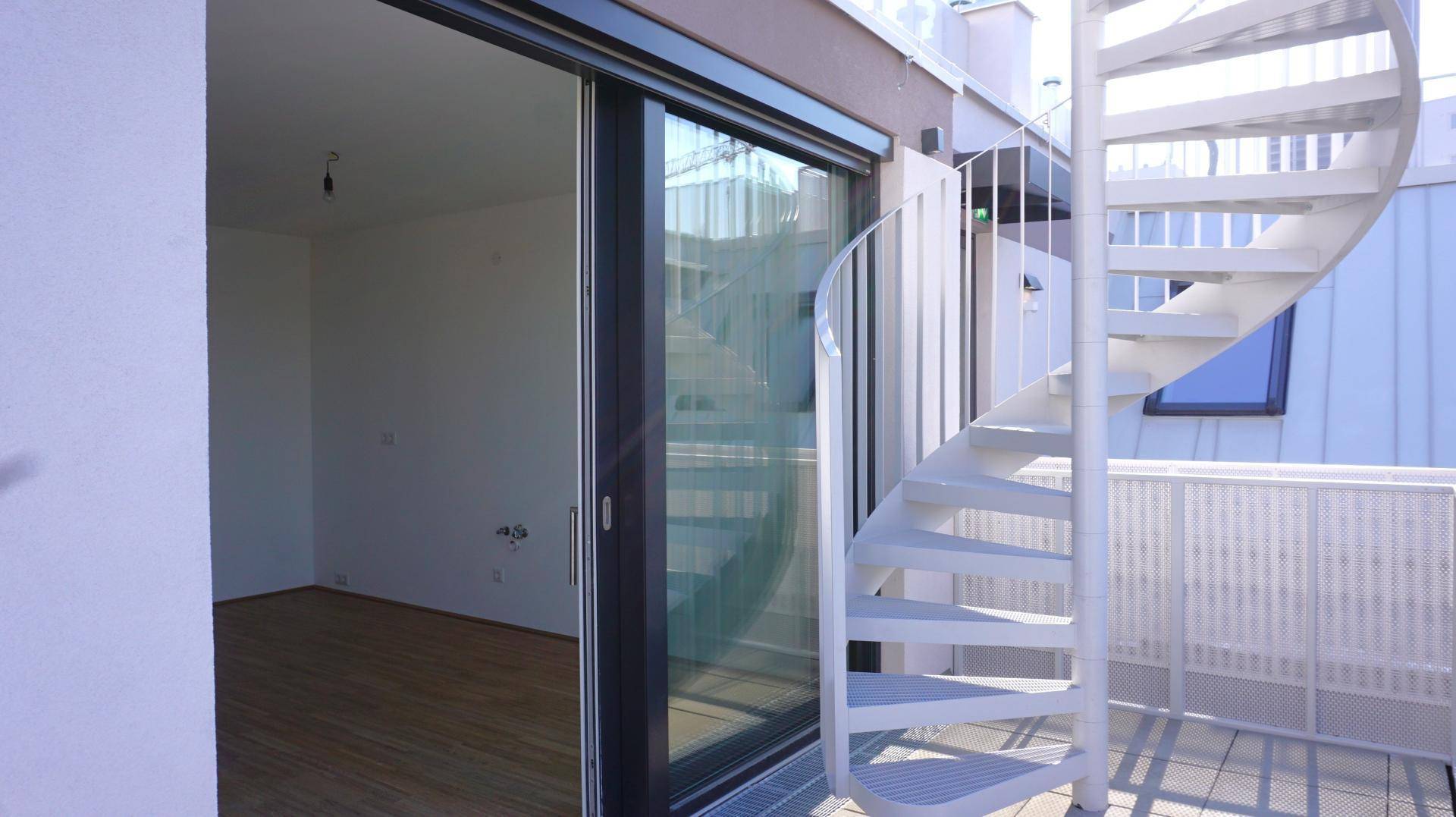 Leerer Innenraum mit Holzboden und Zugang zu einem Balkon über eine große Glasschiebetür.