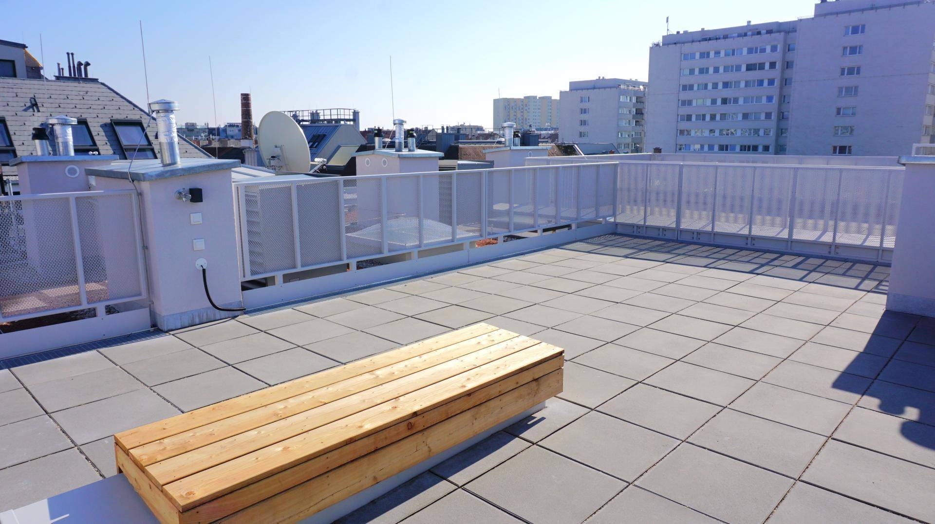 Geräumige Dachterrasse mit Holzsitzbank und weitem Blick über die umliegende Stadtlandschaft.