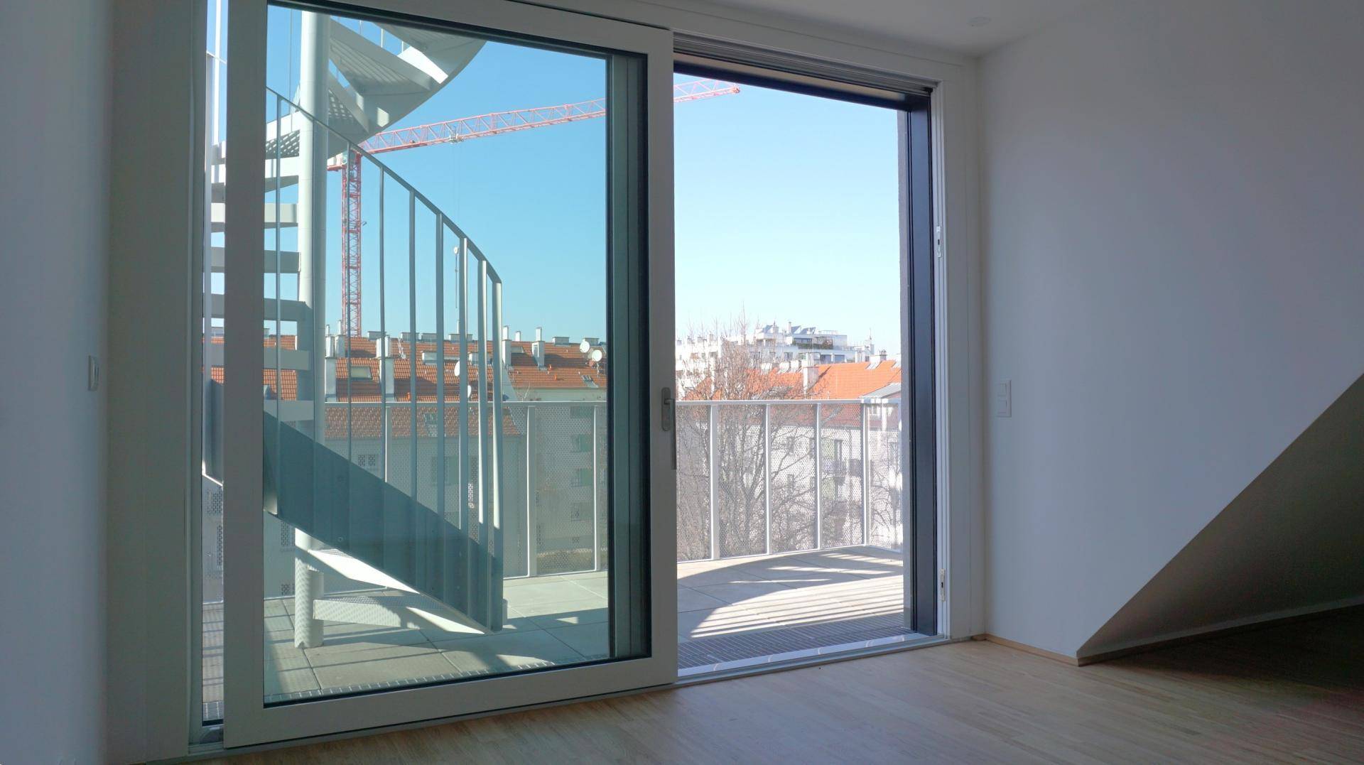 Heller Raum mit Holzboden und weitem Blick über die Stadt von einem Balkon mit Wendeltreppe.