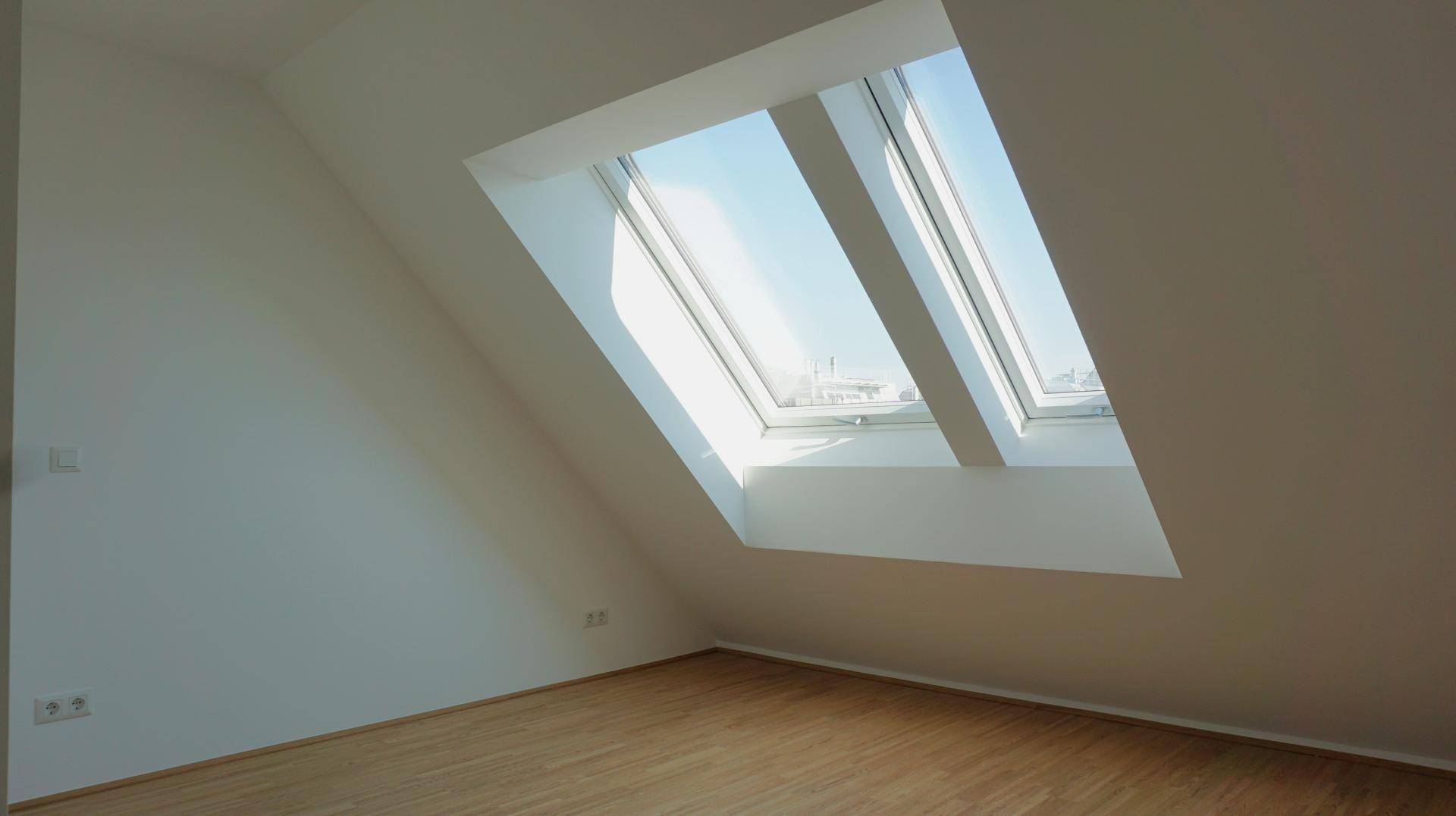 Heller Dachgeschossraum mit schrägen Wänden, Holzboden und großen Dachfenstern für viel Tageslicht.