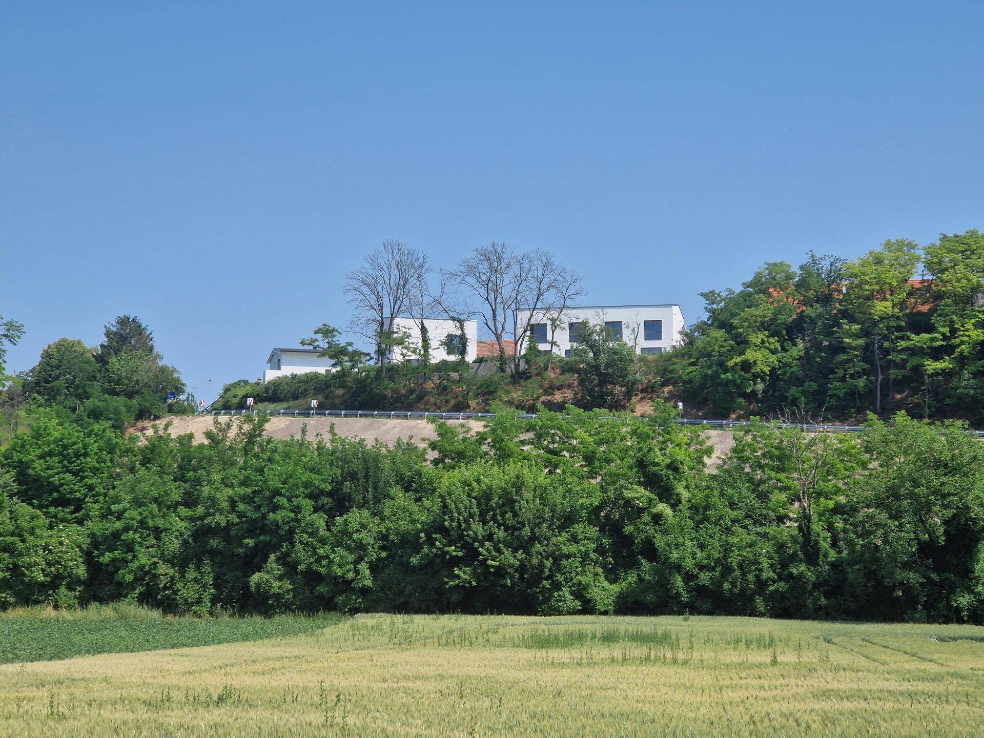 Moderne weiße Gebäude auf einem Hügel, umgeben von üppigem Grün und Feldern unter blauem Himmel.