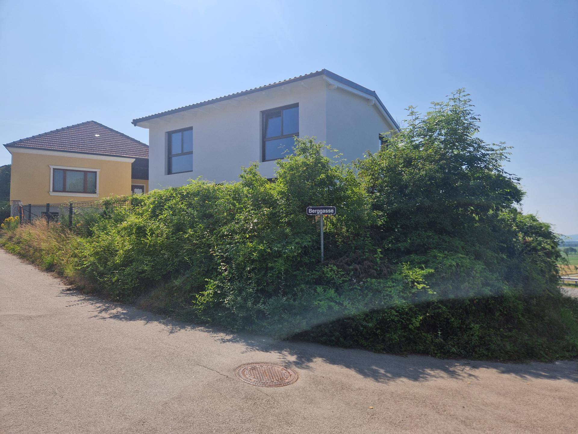 Modernes Einfamilienhaus an einer Straße mit üppiger Vegetation und einem Straßenschild.
